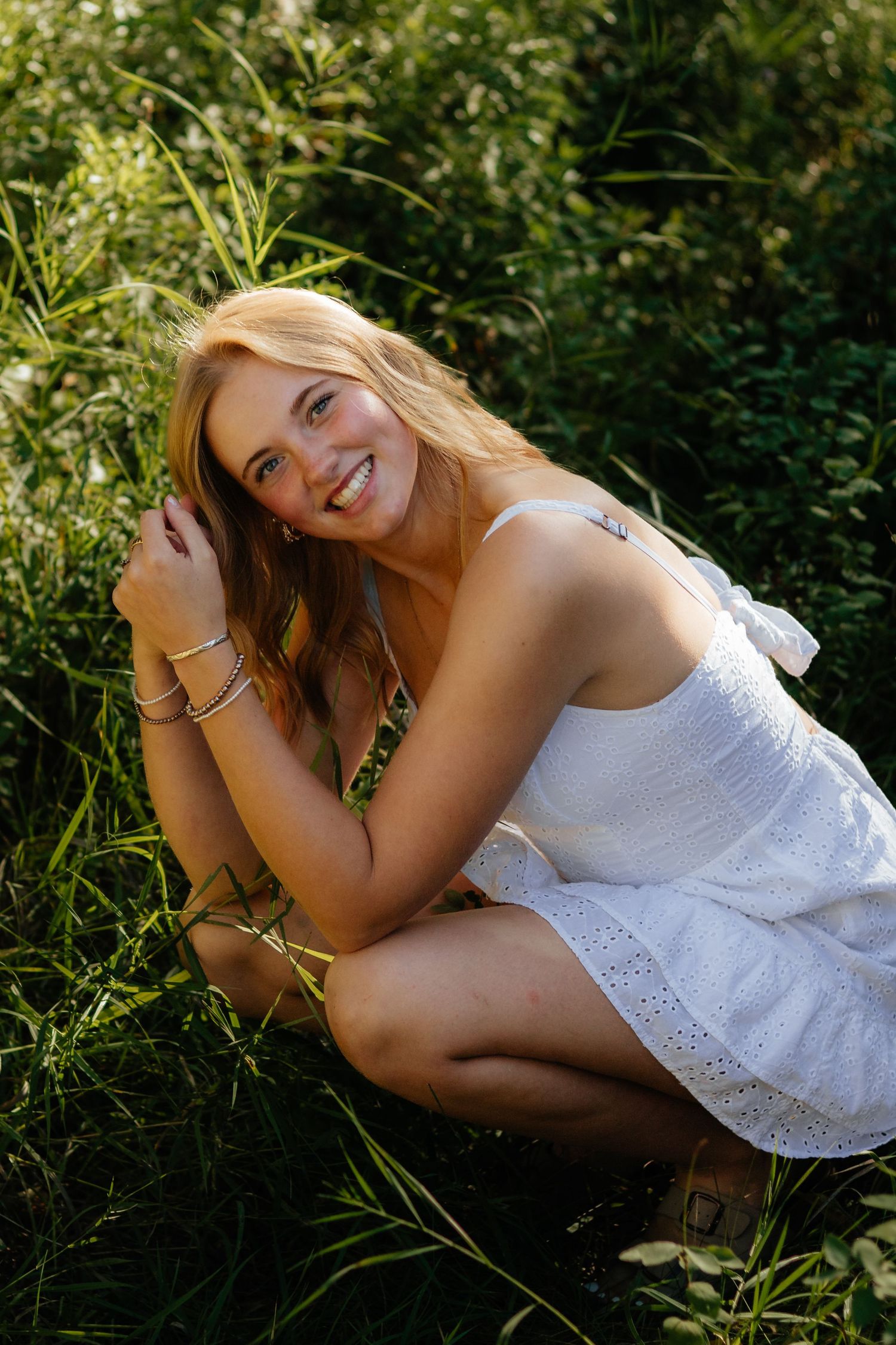 A series of dreamy outdoor portrait photos in white lace dress laying in tall grass and wildflowers.