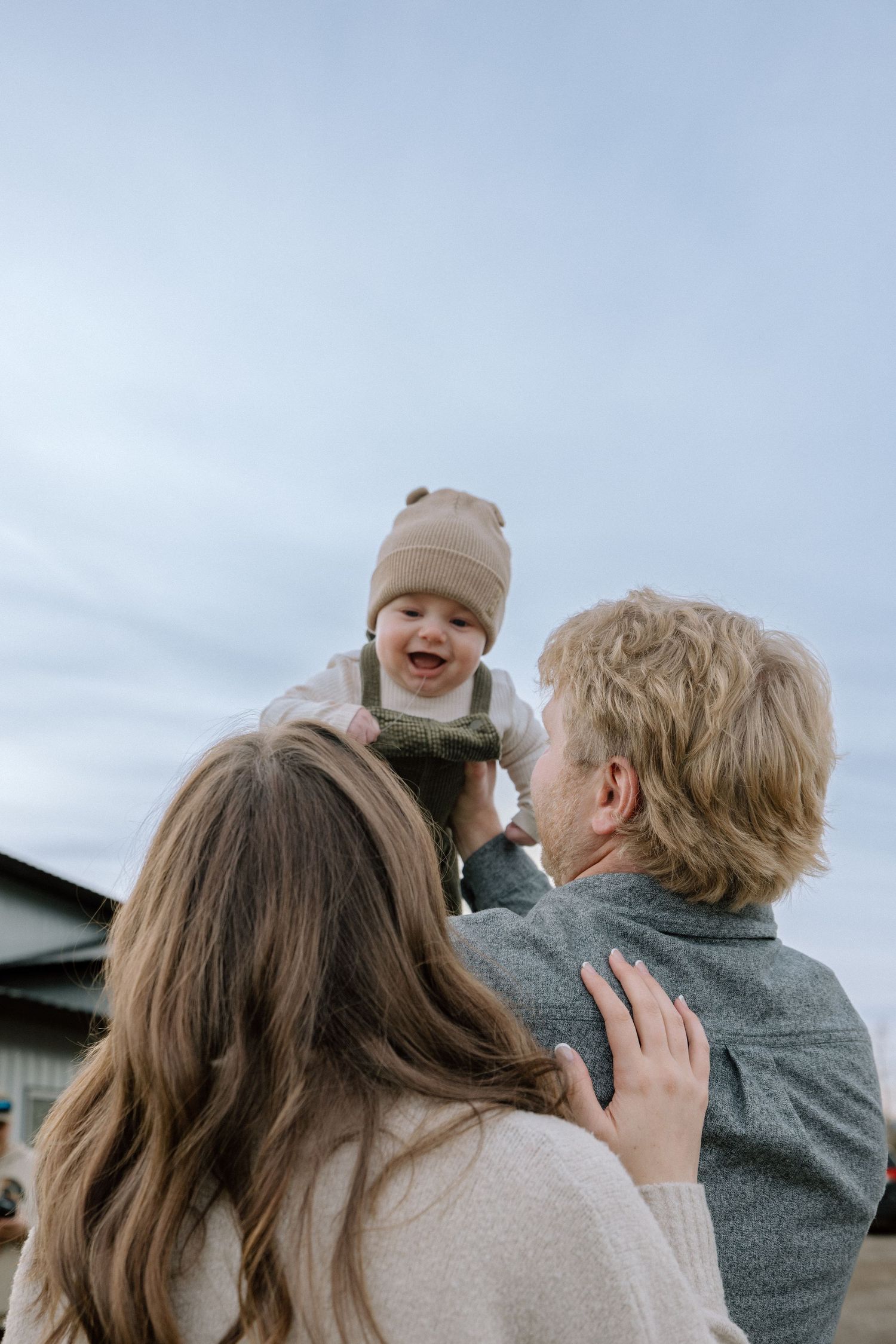A joyful family shares tender moments together outdoors against a bright sky background.