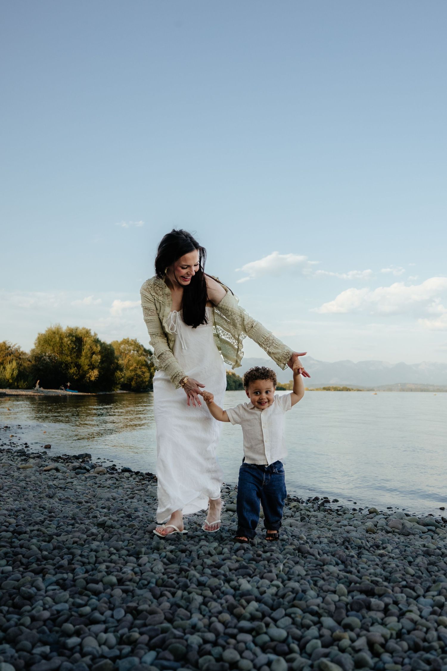 Mother and child share joyful moments together while playing on a rocky beach shore near a serene lake.