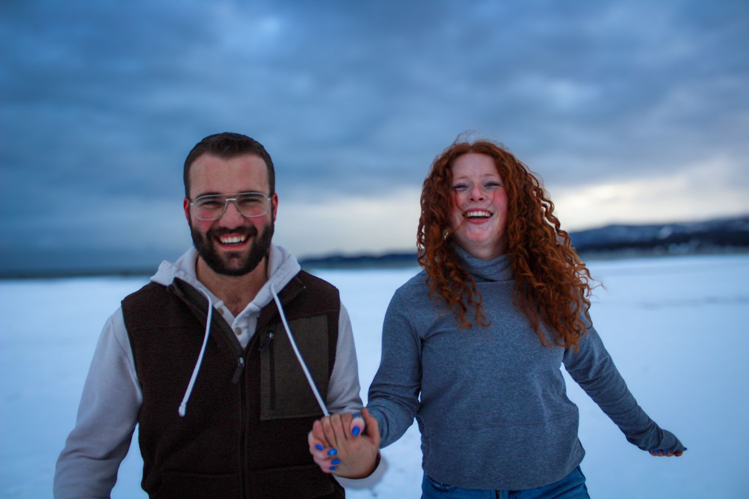 Couple laughing together with scenic water and cloudy sky in the background during outdoor adventure.