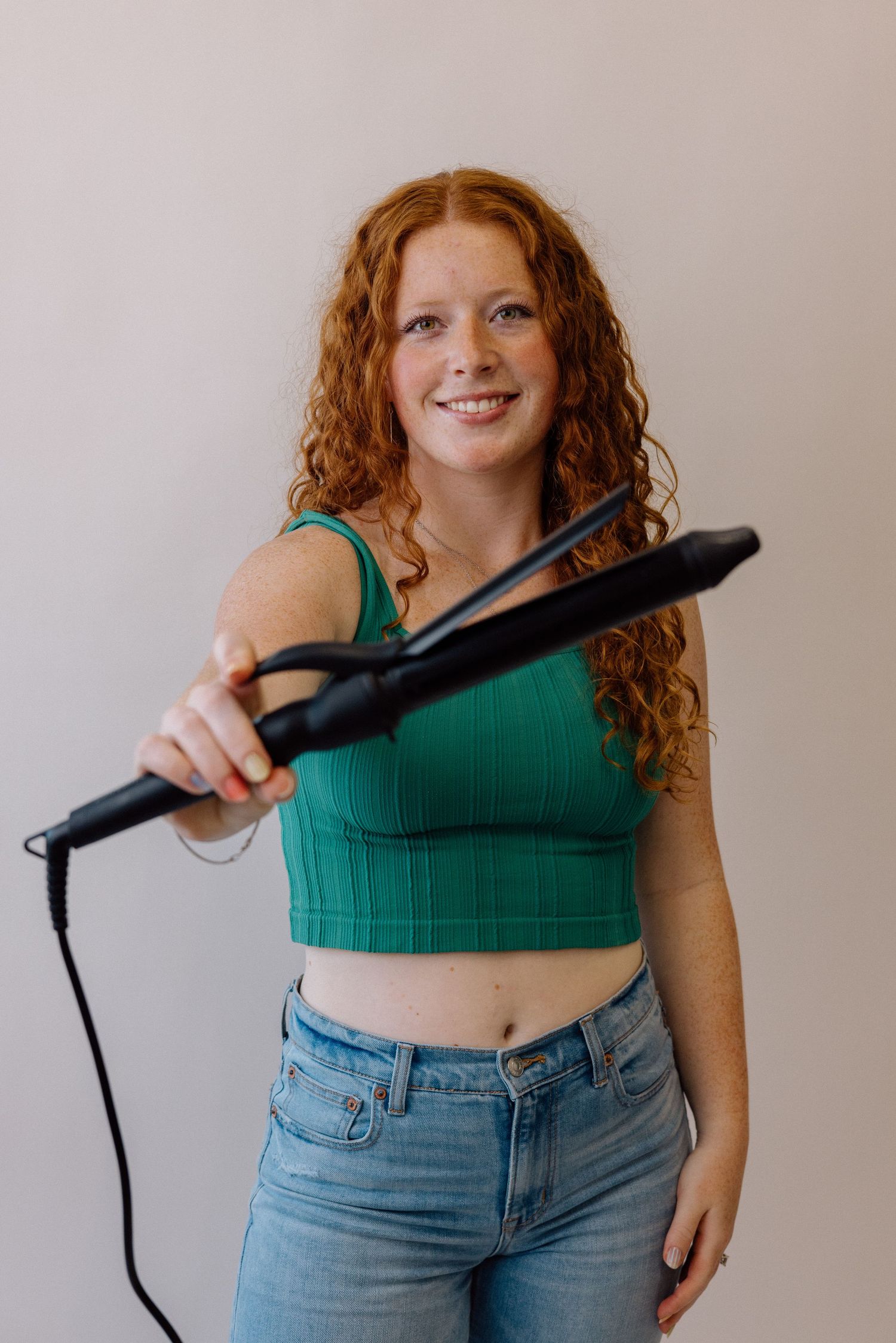 Person in green crop top demonstrates use of hair styling tool.