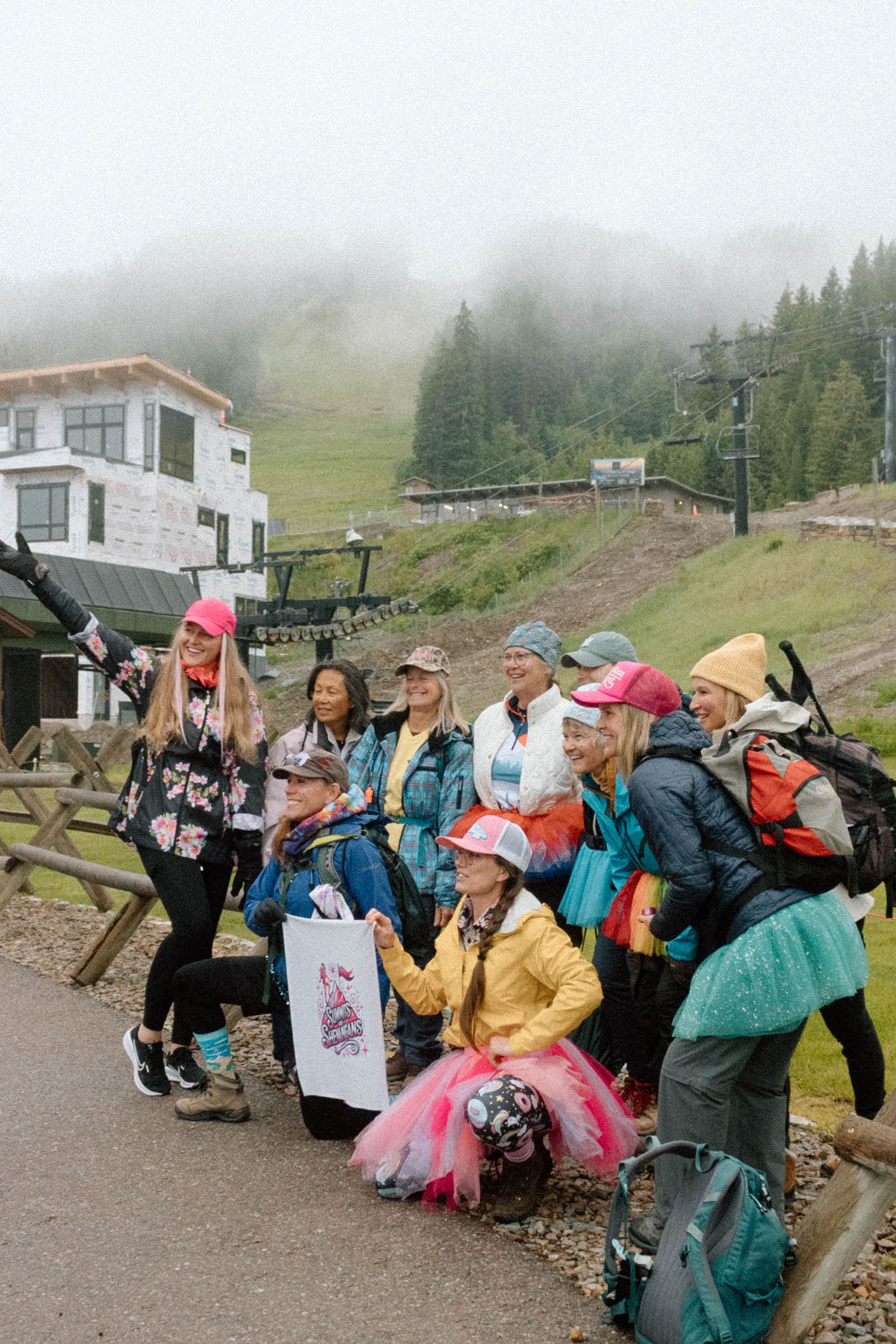 Large group of outdoor enthusiasts gathered at mountain base wearing colorful rain gear.