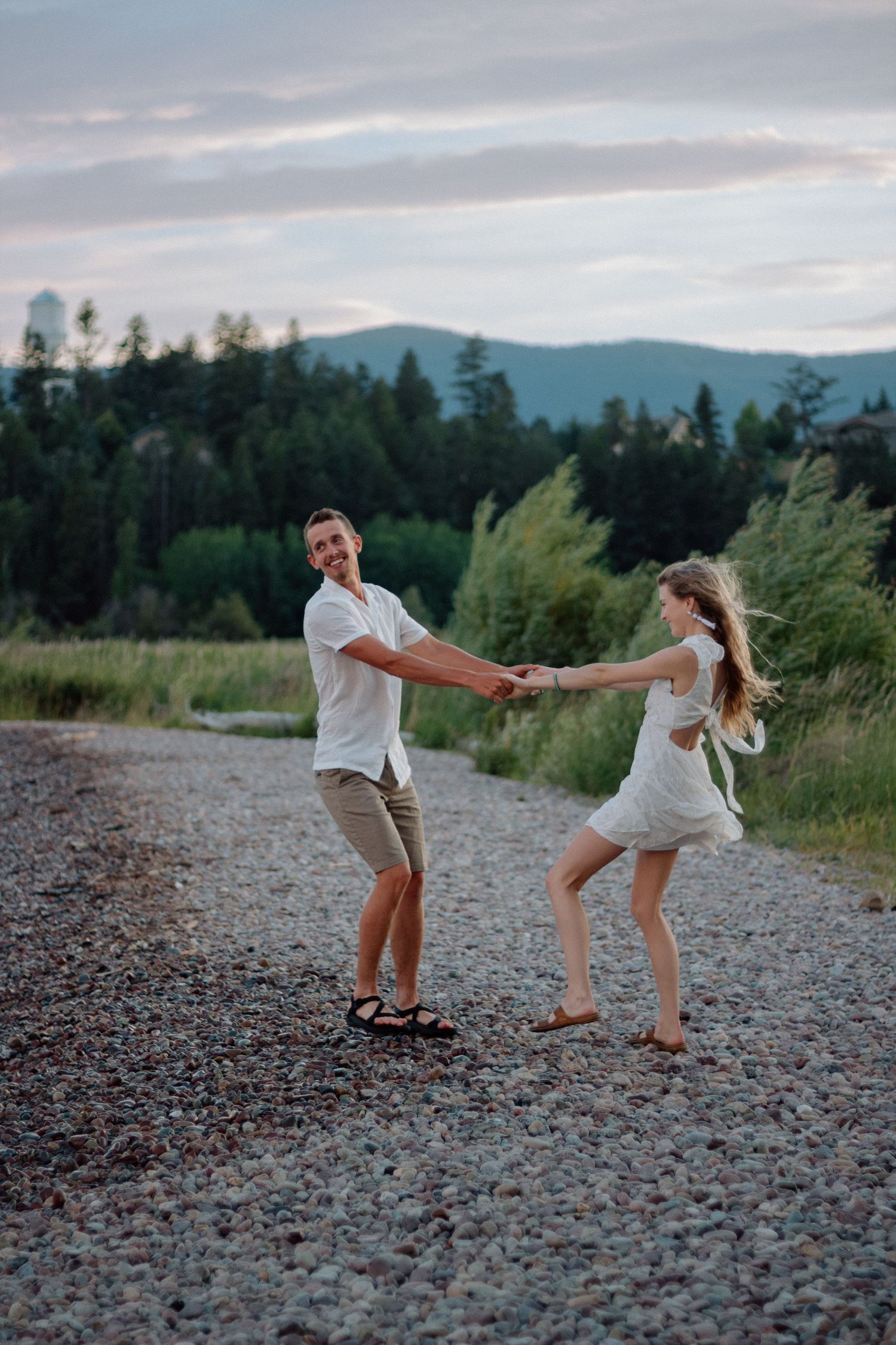 A joyful couple dances and plays in a rocky outdoor setting with mountains in the background.
