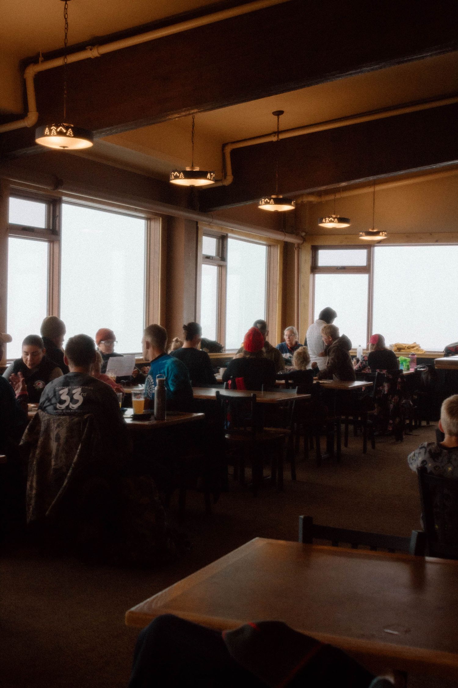 Interior view of a dimly lit mountain lodge restaurant with guests seated at tables.