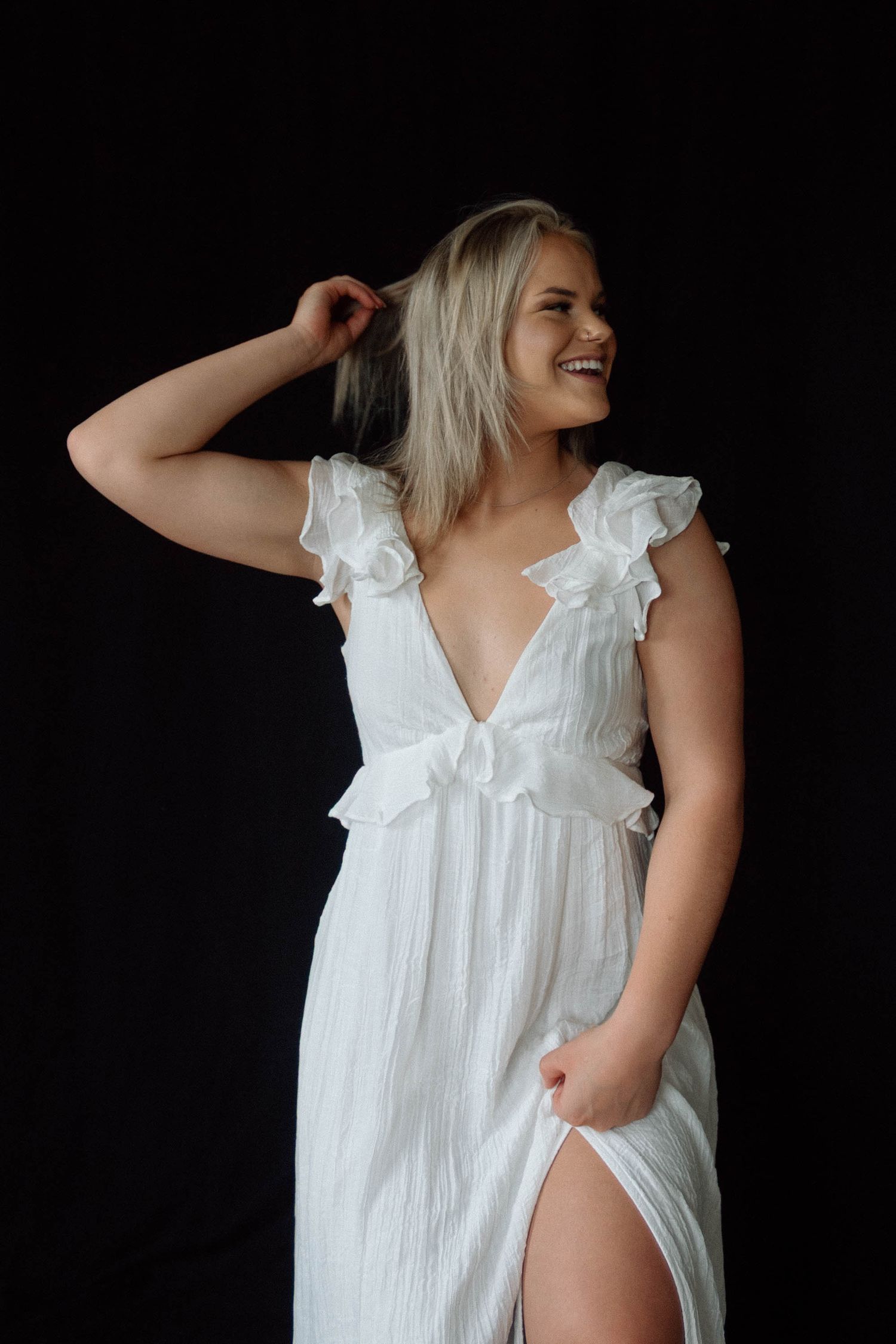 Model wearing a white ruffled cotton nightgown poses playfully against dark background in lifestyle photoshoot series.