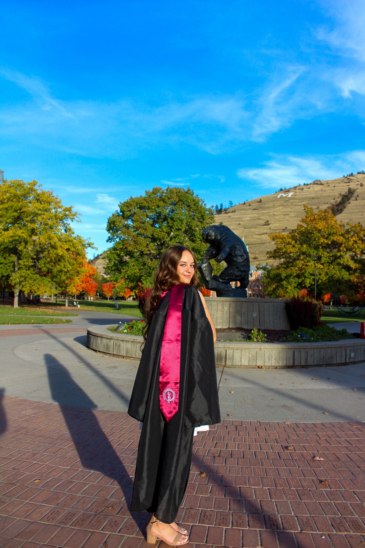A series of graduation photos showing someone in a black cap and gown with pink attire underneath posing on a brick plaza.