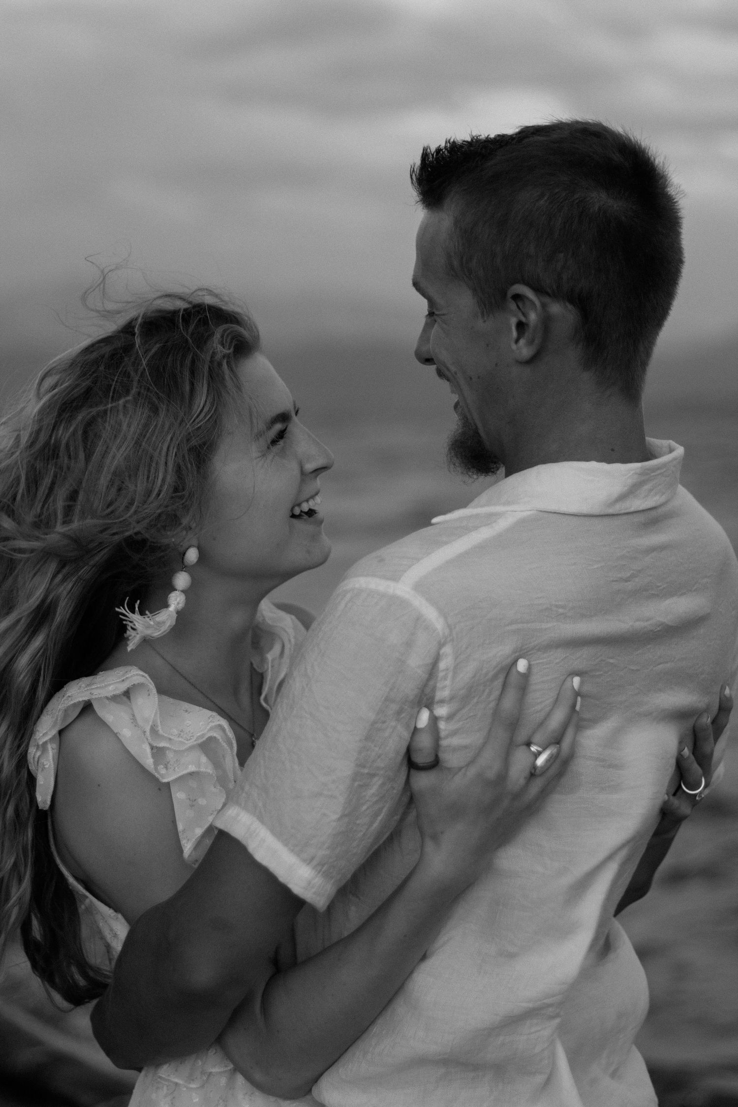 A black and white photo captures an intimate moment between a couple on the shoreline.