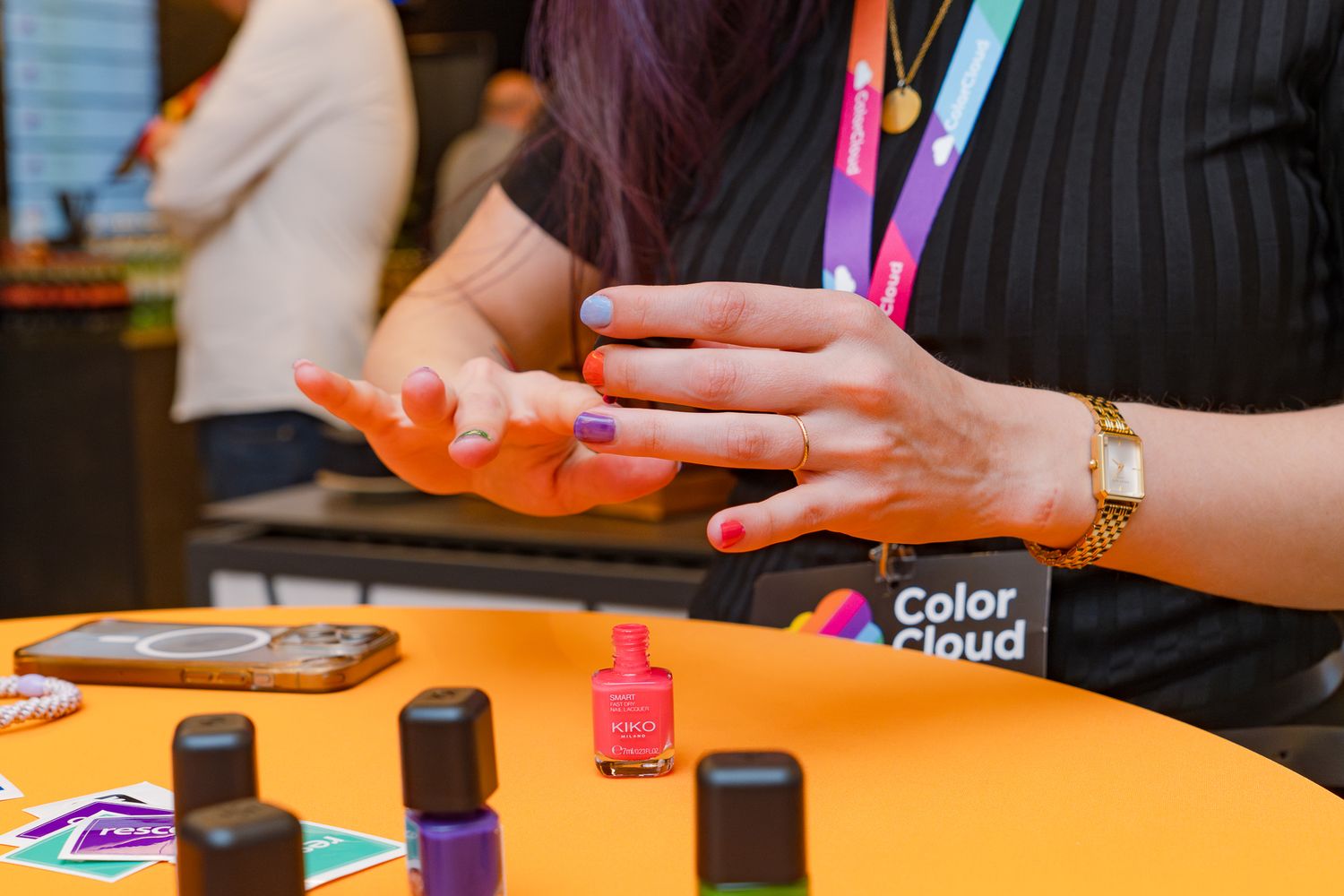 Eine Hand mit bunt lackierten Nägel trägt an einem gelben Stehtisch weiteren Nagellack auf