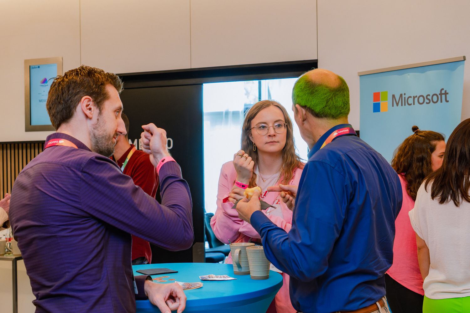 Drei Teilnehmende zeigen sich gegenseitig bunte Armbänder während der Pause im Foyer der ColorCloud Konferenz