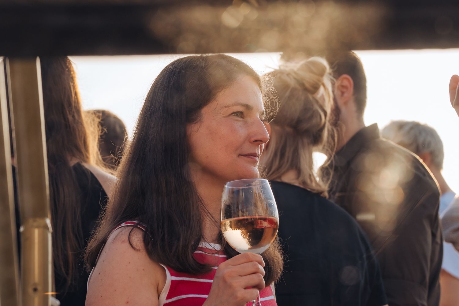 Junge Frau im Licht der Abendsonne mit Weinglas in der Hand hinter einer Glasscheibe
