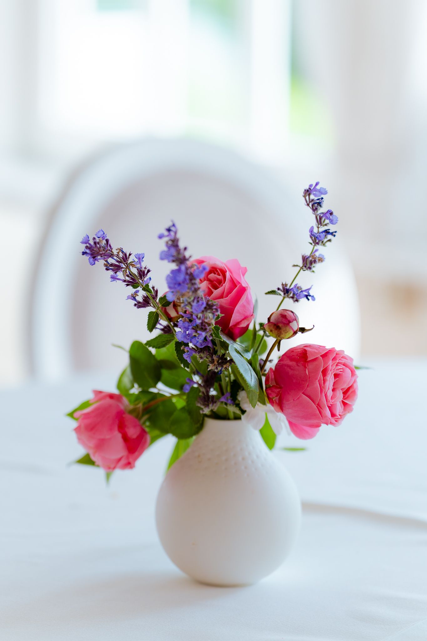 Blumenvase mit Blumenstrauß auf weiß gedecktem Tisch
