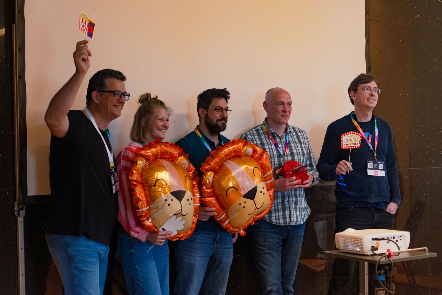 Ein Team präsentiert beim ColorCloud PromptAthon Ergebnisse vor anderen Teilnehmenden und hält dabei bunte Löwen-Luftballons in der Hand
