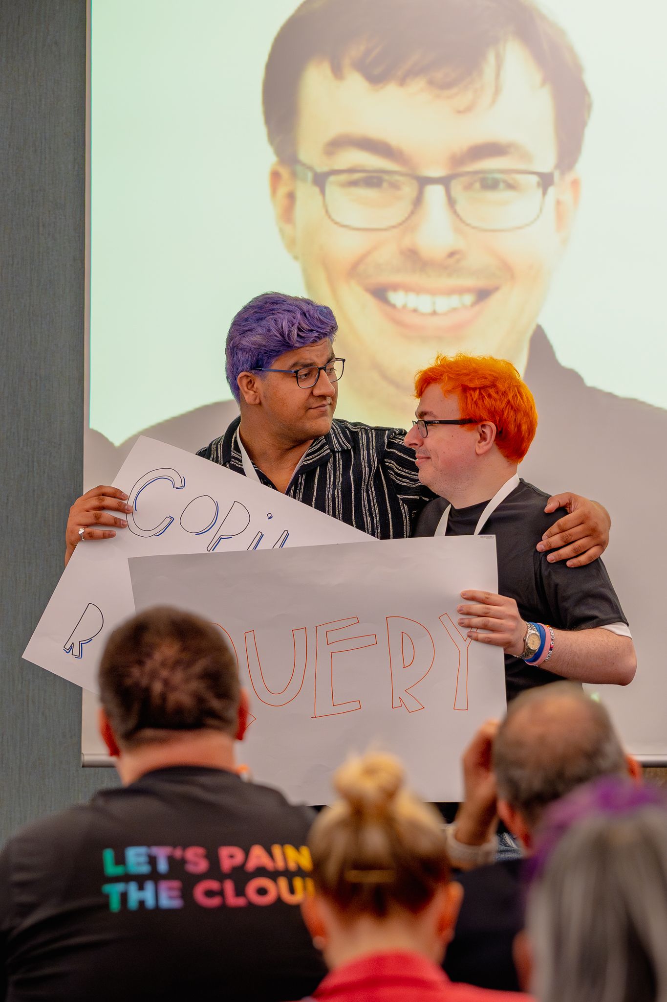 Zwei Keynote-Speaker umarmen sich an den Schultern und halten weiße Schilder hoch während der Eröffnungsrede der ColorCloud Konferenz