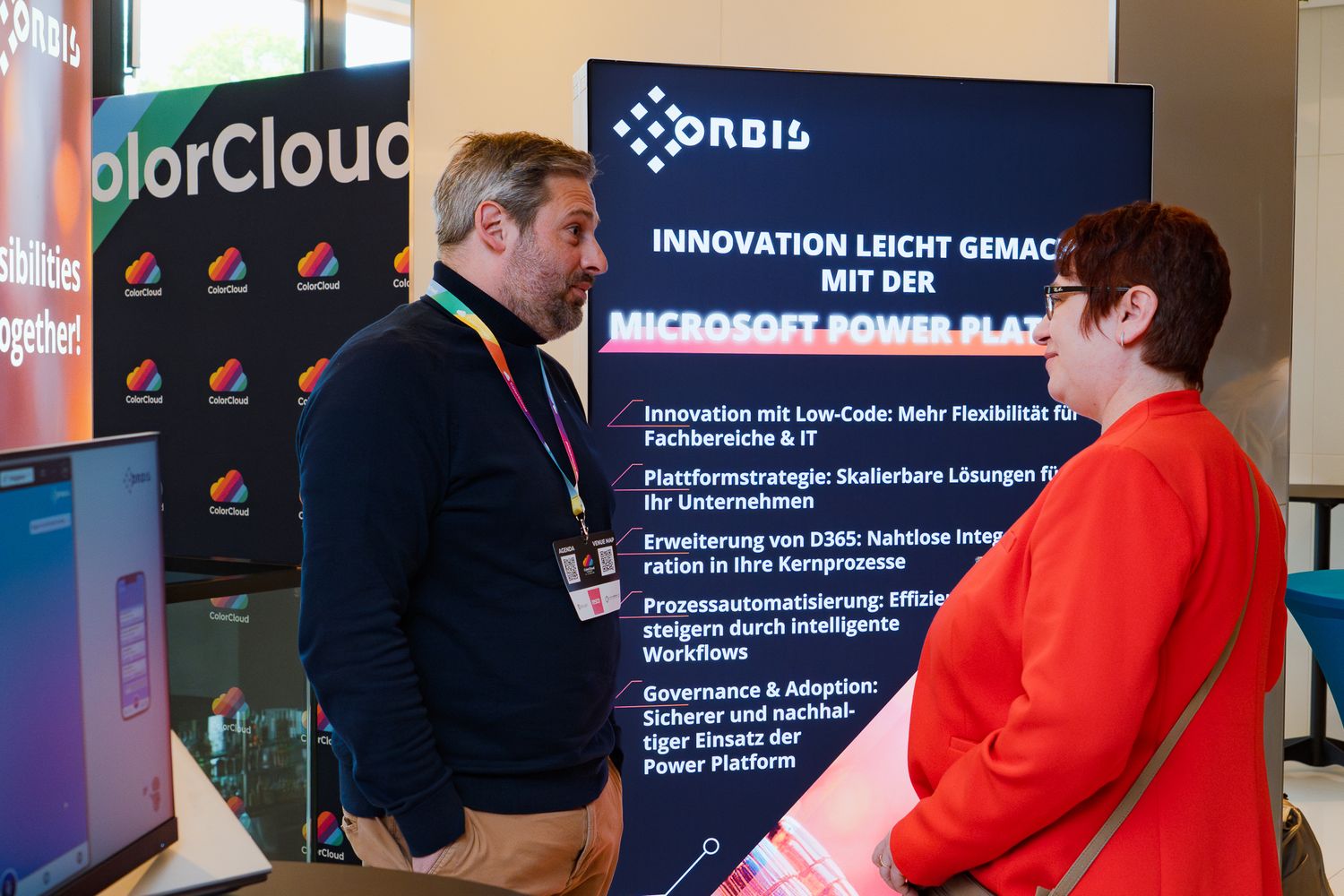 Zwei Teilnehmer an der ColorCloud-Konferenz 2025 unterhalten sich am Sponsorenstand von Orbis