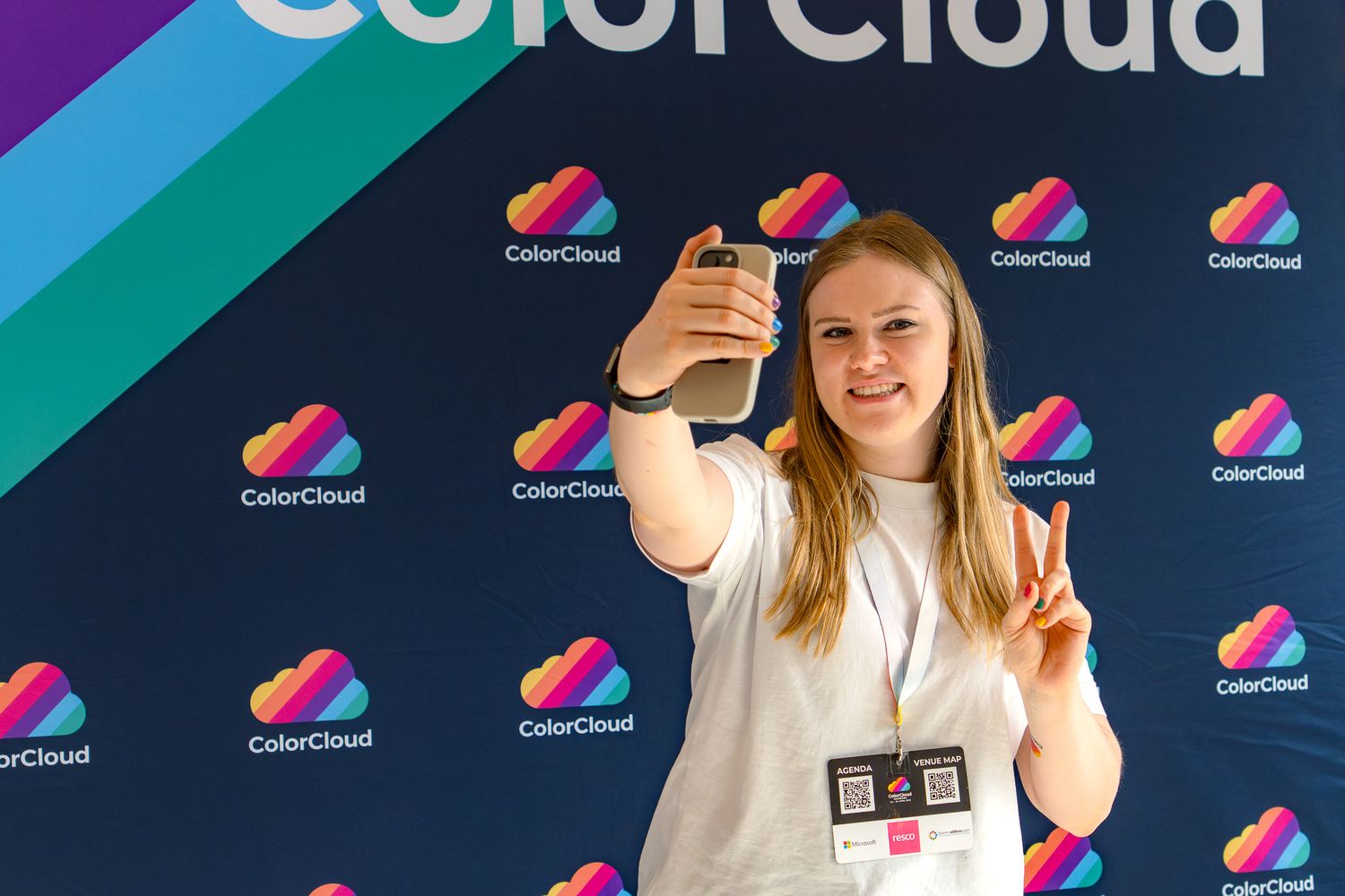 Paulina Meißner, Mitorganisatorin der ColorCloud-Konferenz posiert vor einer Fotowand und macht ein Selfie mit Victory-Handzeichen