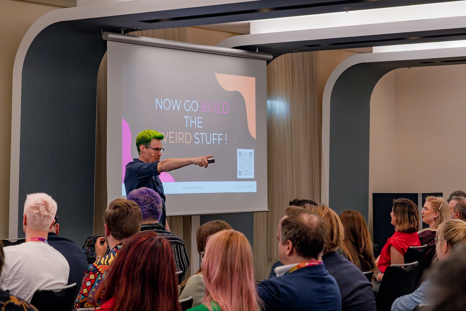 Scott Durow zeigt zum Schluss einer Rede mit ausgestrecktem Arm nach vorne, auf einer Leinwand seht 'Now go build the weird stuff'