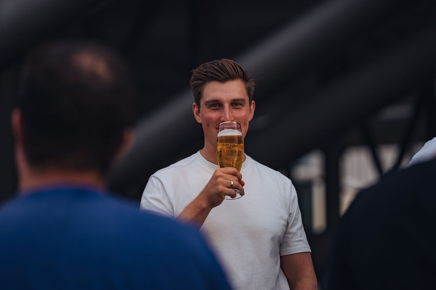 Junger Mann im weißen T-Shirt trinkt aus einem Bierglas.
