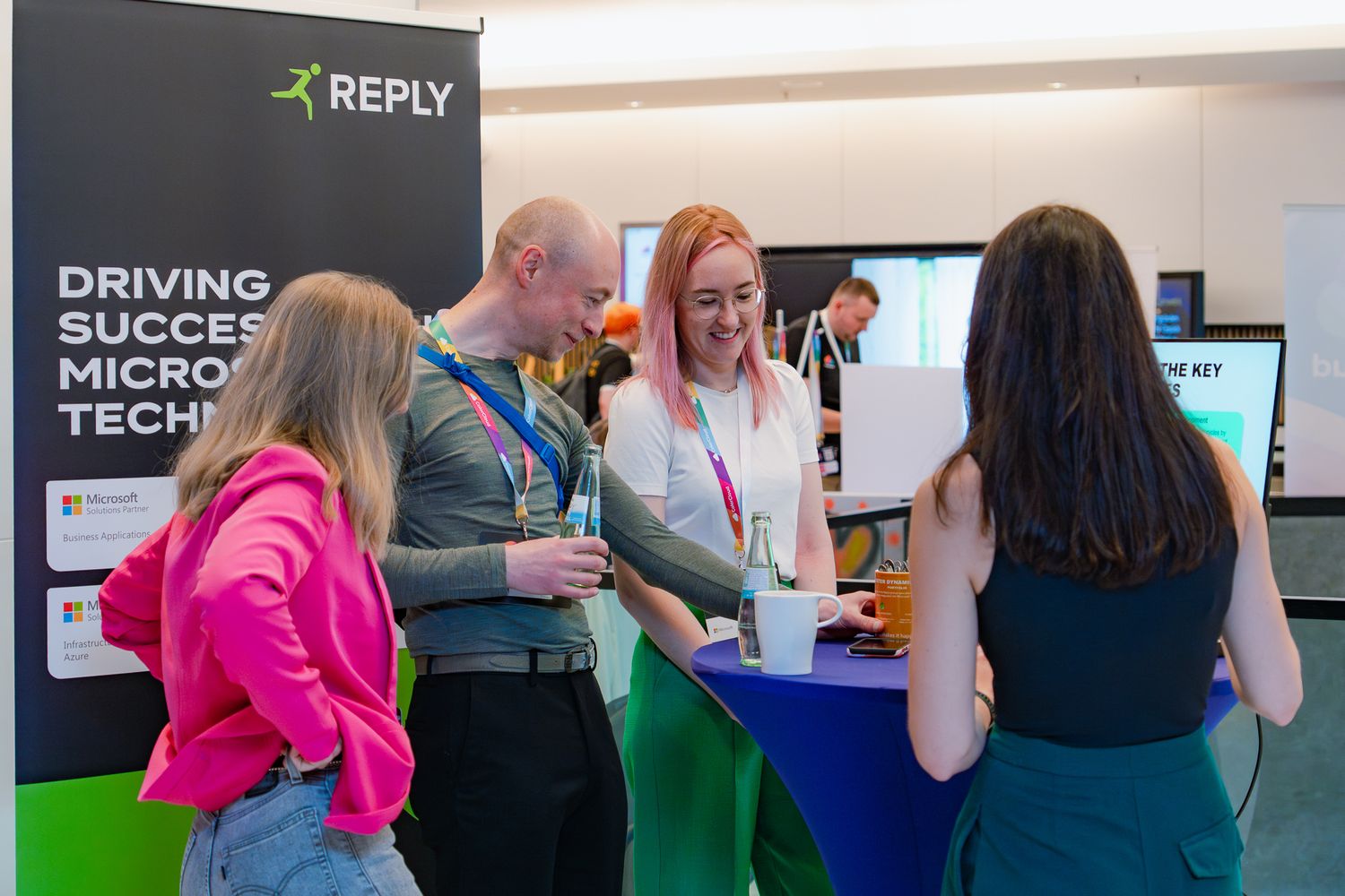 Vier Personen stehen am Sponsorenstand von Reply im Foyer der ColorCloud-Konferenz und unterhalten sich
