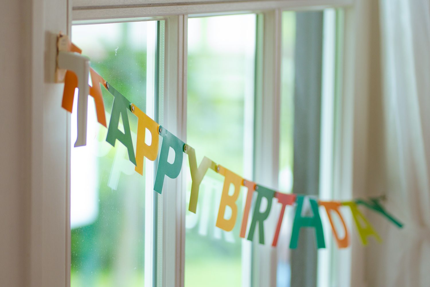 Eine bunte Happy Birthday-Girlande, die am Fenster angebracht ist