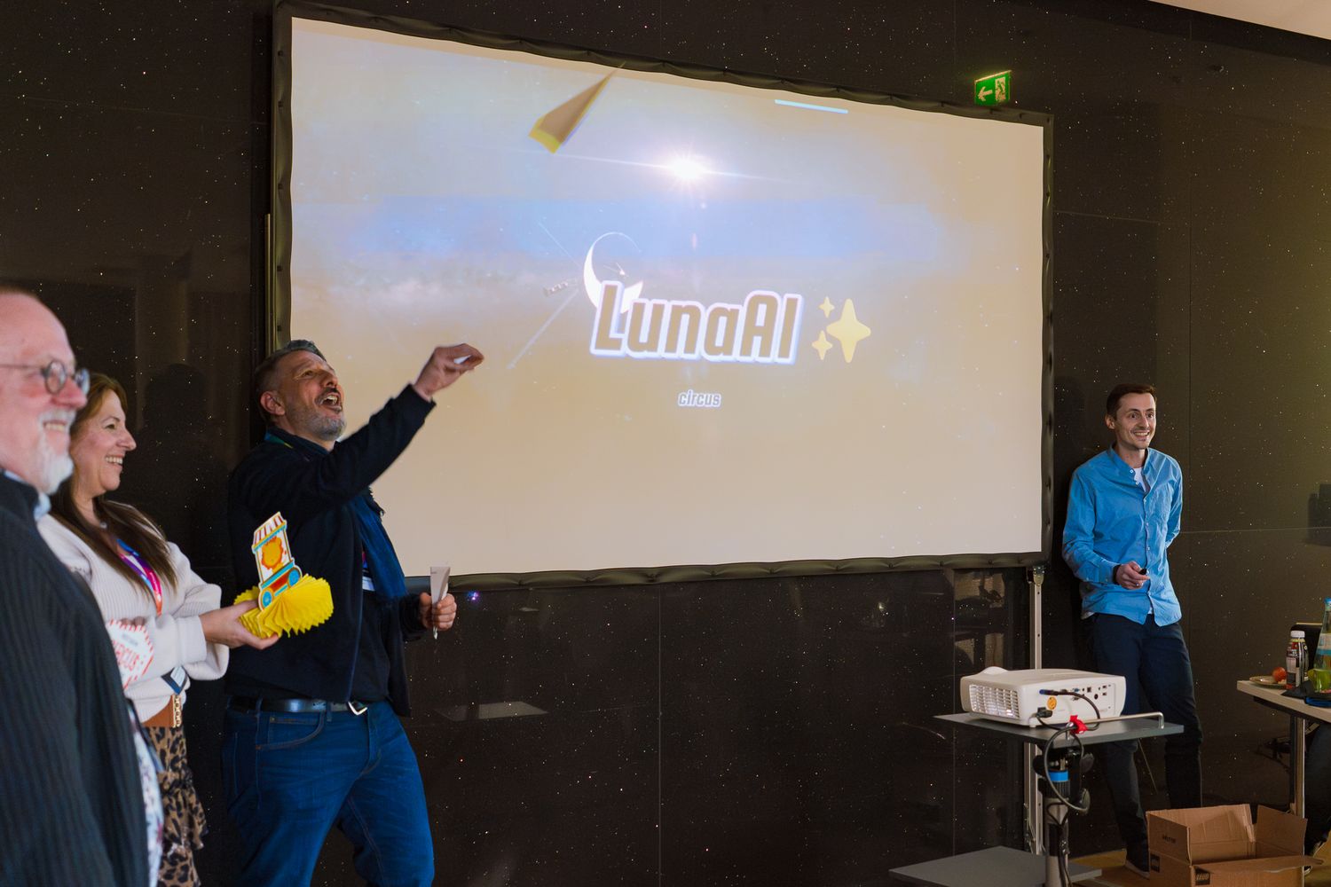 Ein Team präsentiert beim ColorCloud PromptAthon Ergebnisse vor anderen Teilnehmenden und lässt ein Papierflugzeug fliegen