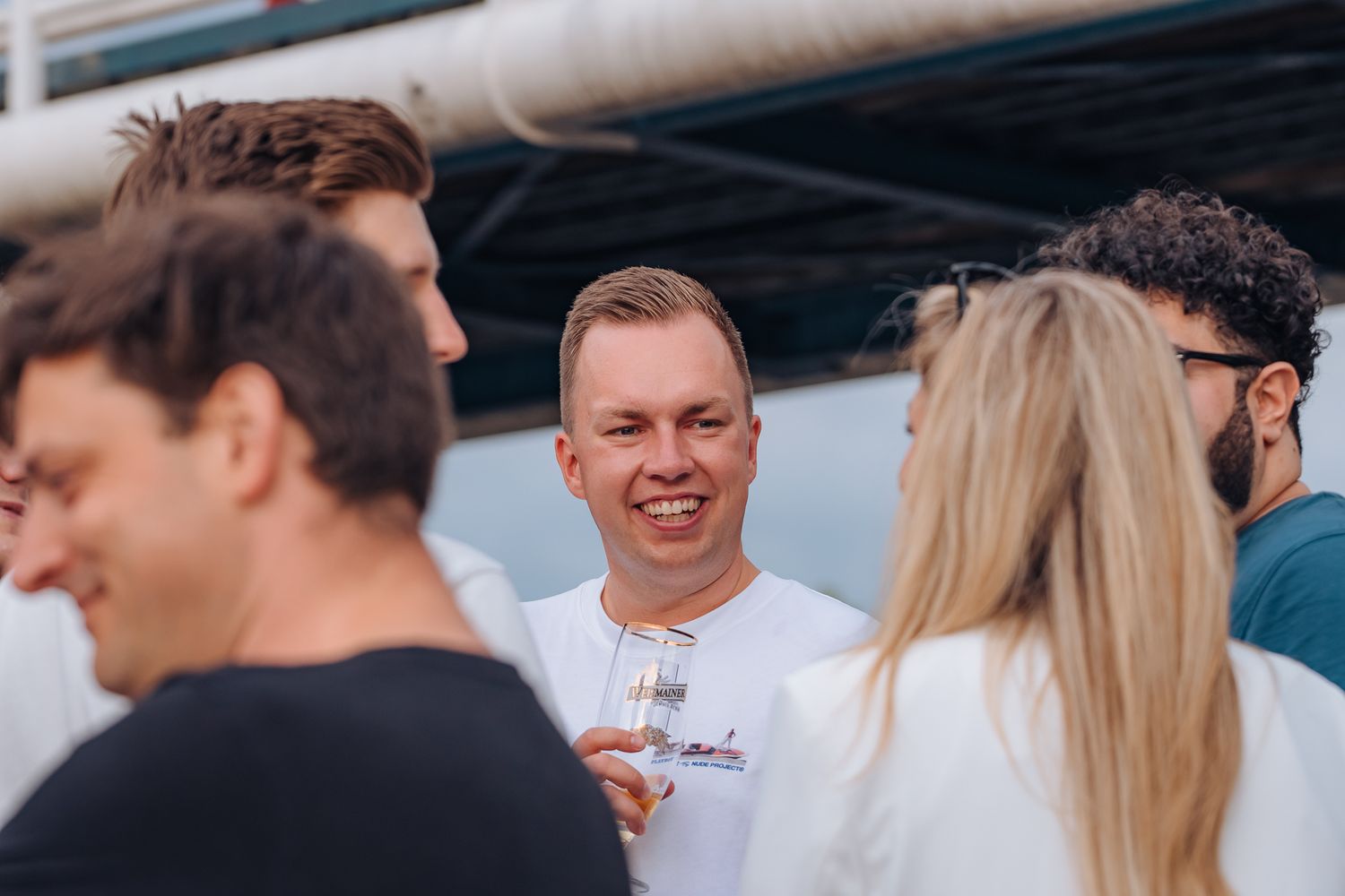 Junger lächelnder Mann mit Bierglas unterhält sich mit seinen Kolleginnen und Kollegen