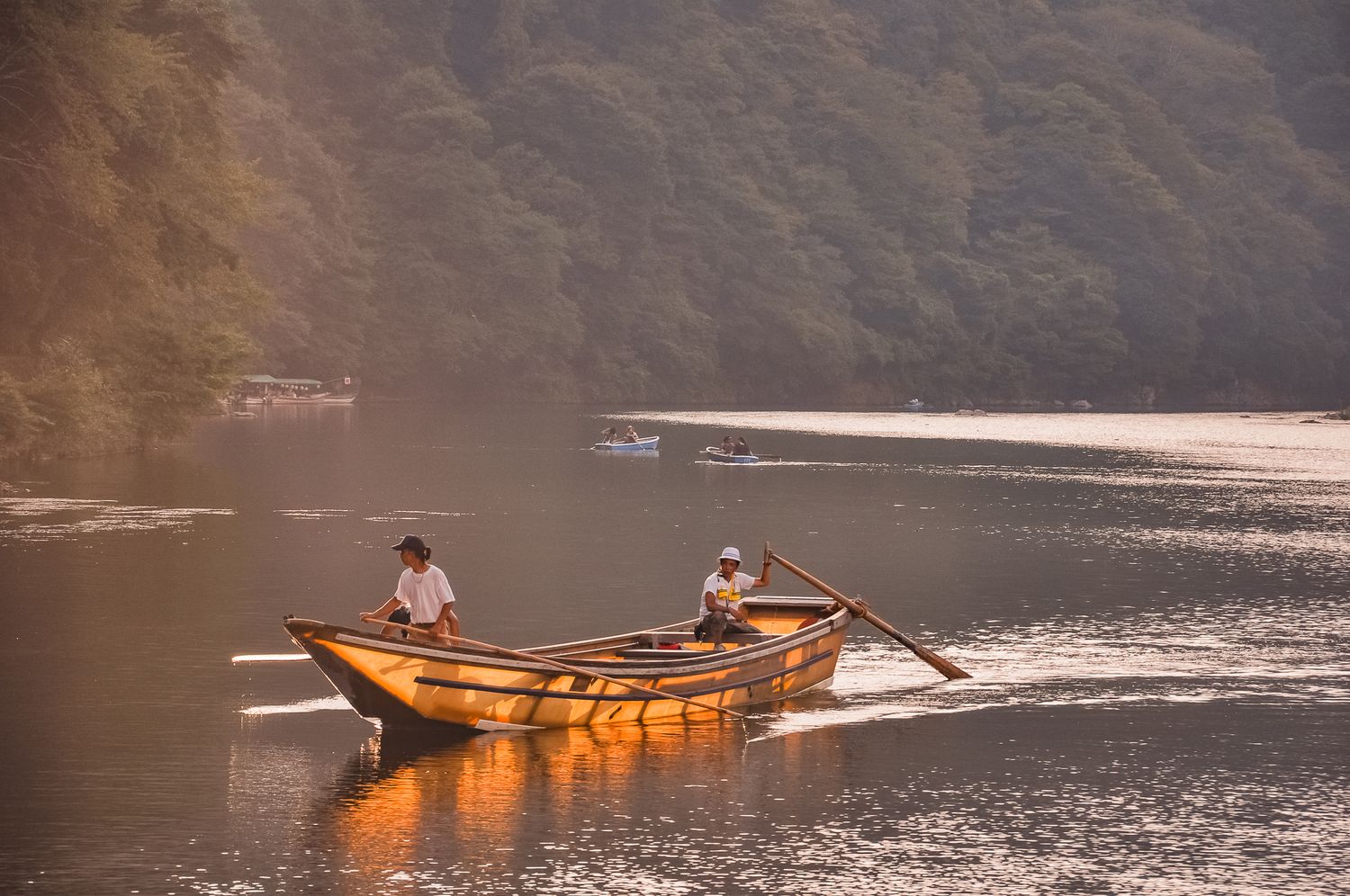 Zwei japanische Männer rudern ein traditionelles Holzboot auf dem Katsura Fluss in Arashiyama bei warmem Abendlicht