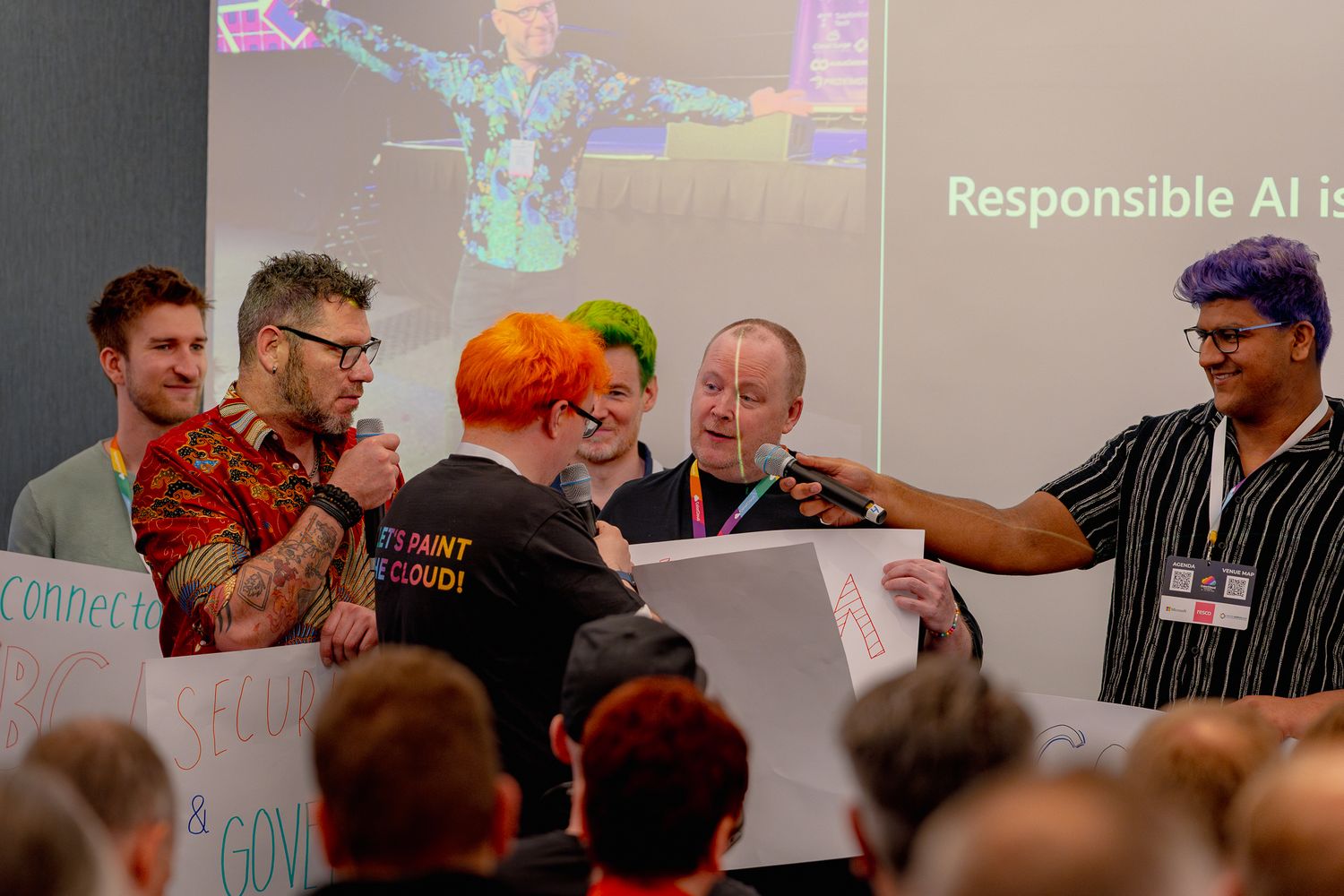 Mehrere Keynote-Speaker der ColorCloud-Konferenz stehen mit weißen Schildern und Mikrofonen vor dem Publikum