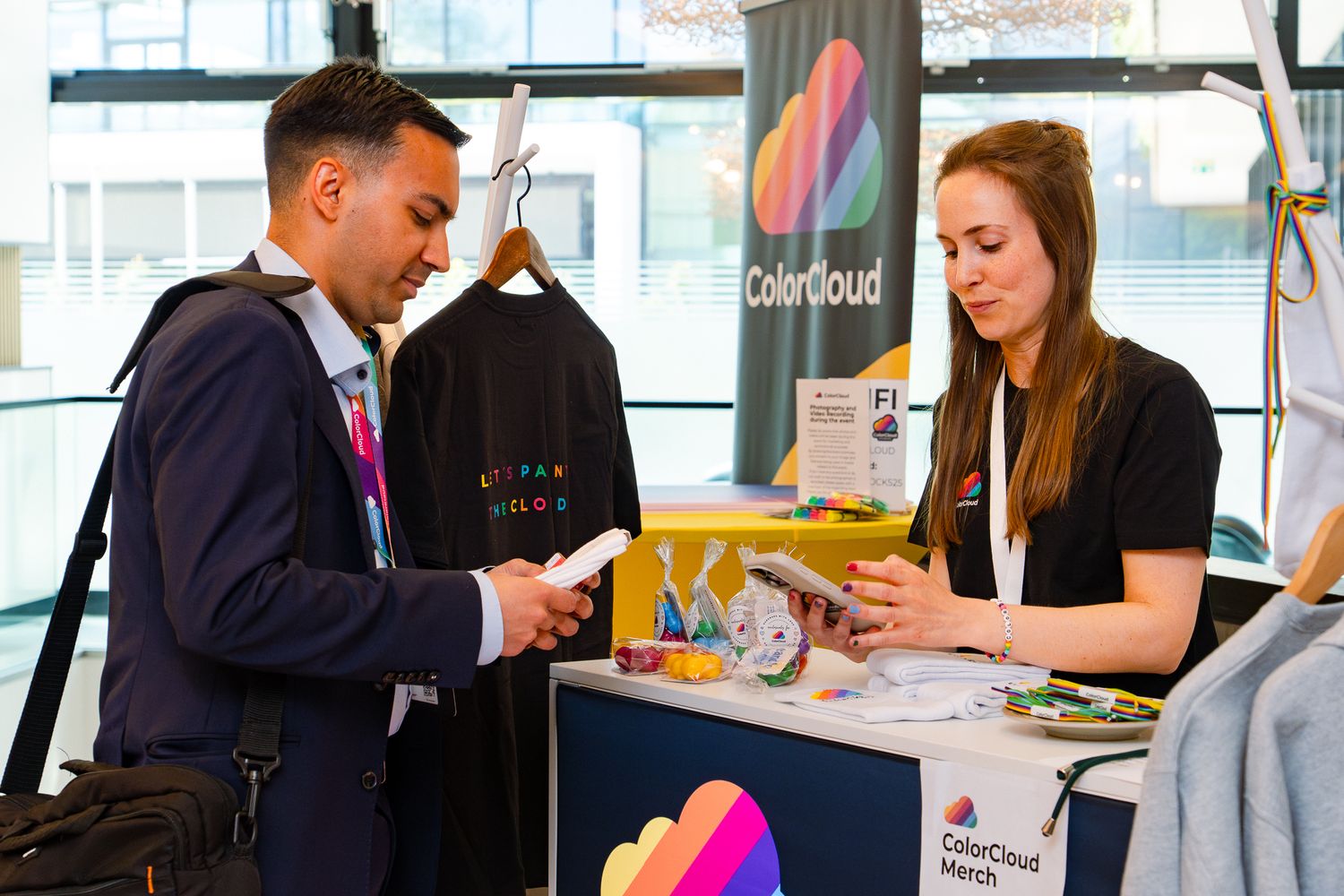 Ein Teilnehmer an der ColorCloud-Konferenz 2025 kauft am Merch-Stand im Foyer ein Produkt und bezahlt bei einer Mitarbeiterin