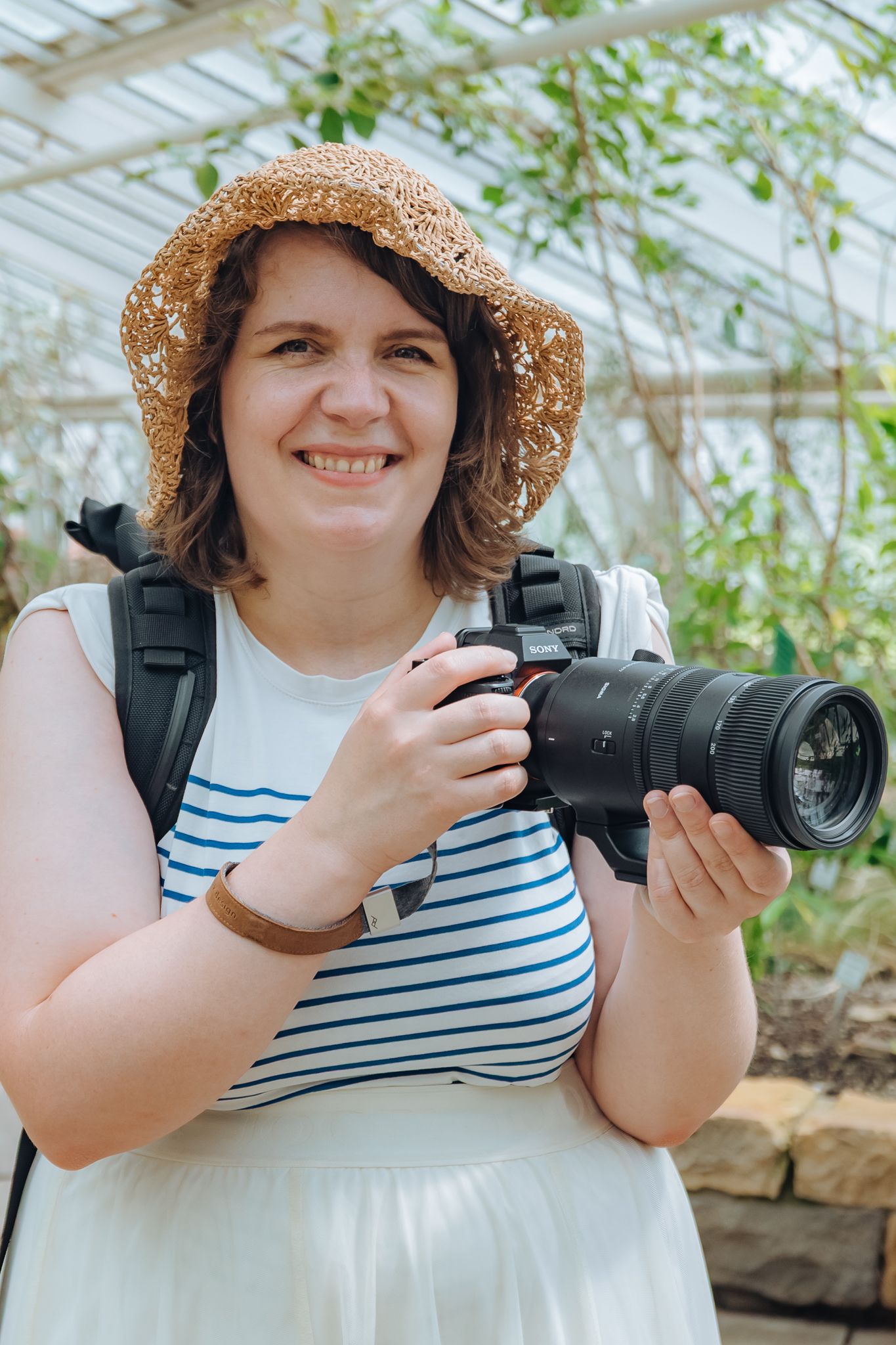 Fotografin Jana Spychalski trägt einen Strohhut und sommerliche Kleidung und hält ihre Sony-Kamera in beiden Händen