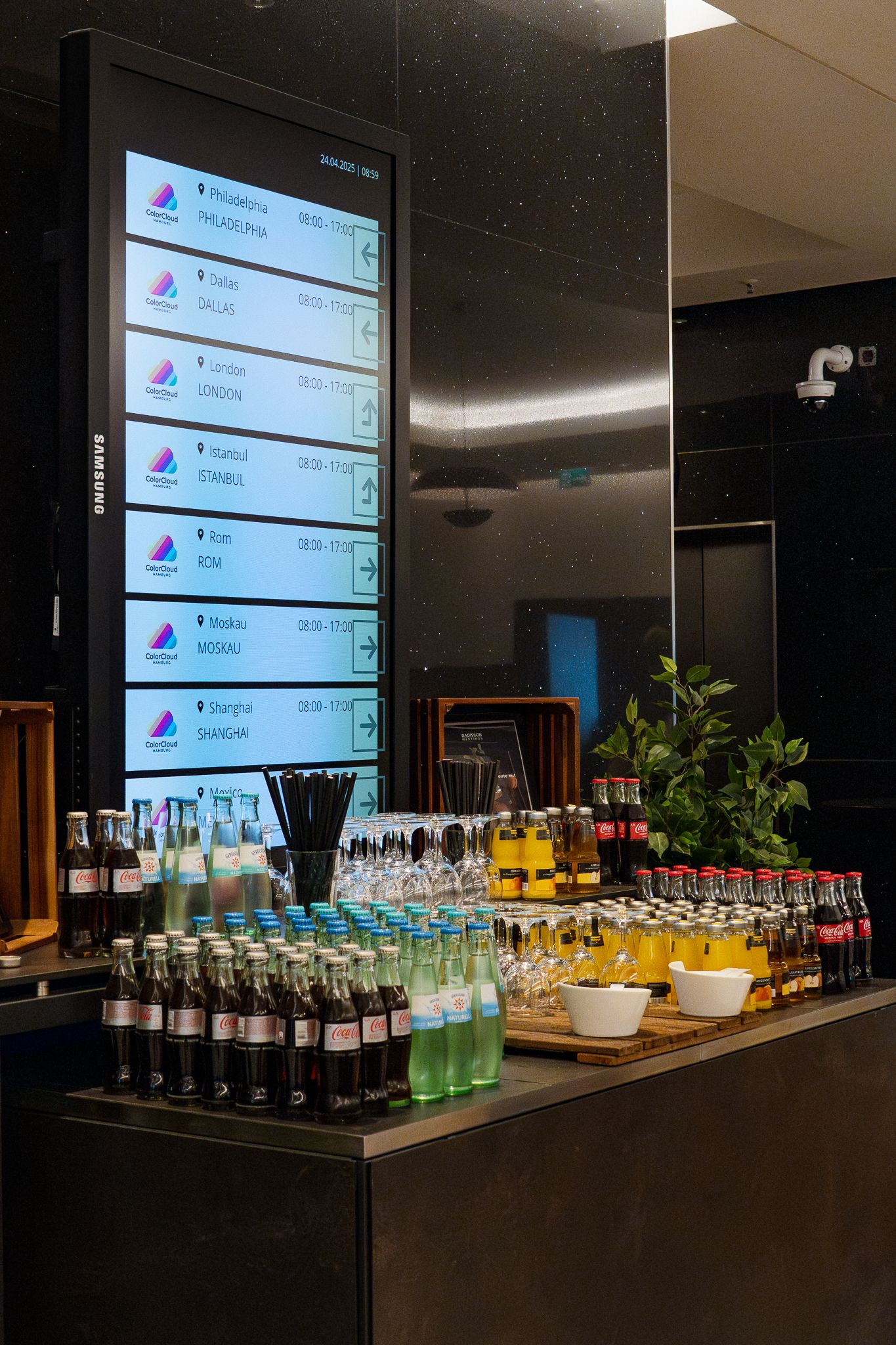 Getränkebuffet mit Softdrinks, Wasser, Saft und Gläsern vor einer Anzeigetafel im Konferenzfoyer