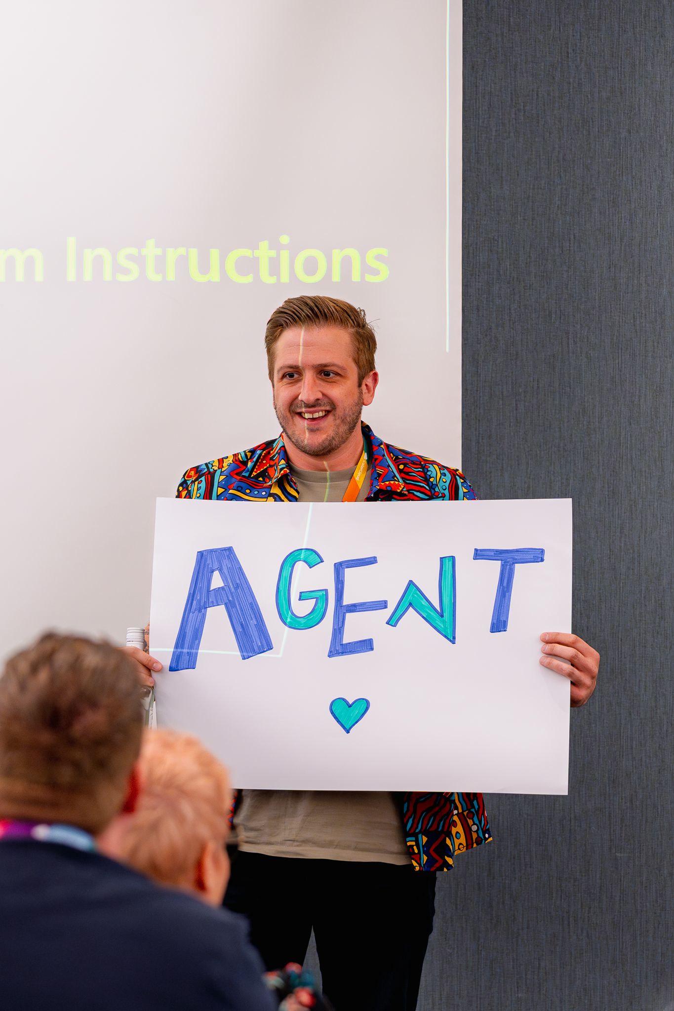 William Dorrington hält während der Keynote auf der ColorCloud Konferenz 2025 ein weißes Schild mit der Aufschrift 'Agent' hoch