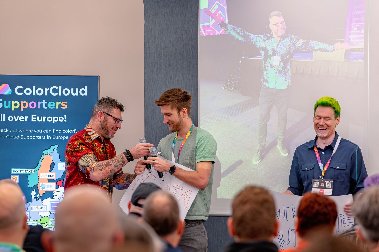 Christ Huntingford, Tine Staric und Scott Durow halten zusammen die Keynote auf der ColorCloud 2025 und halten weiße Schilder in den Händen