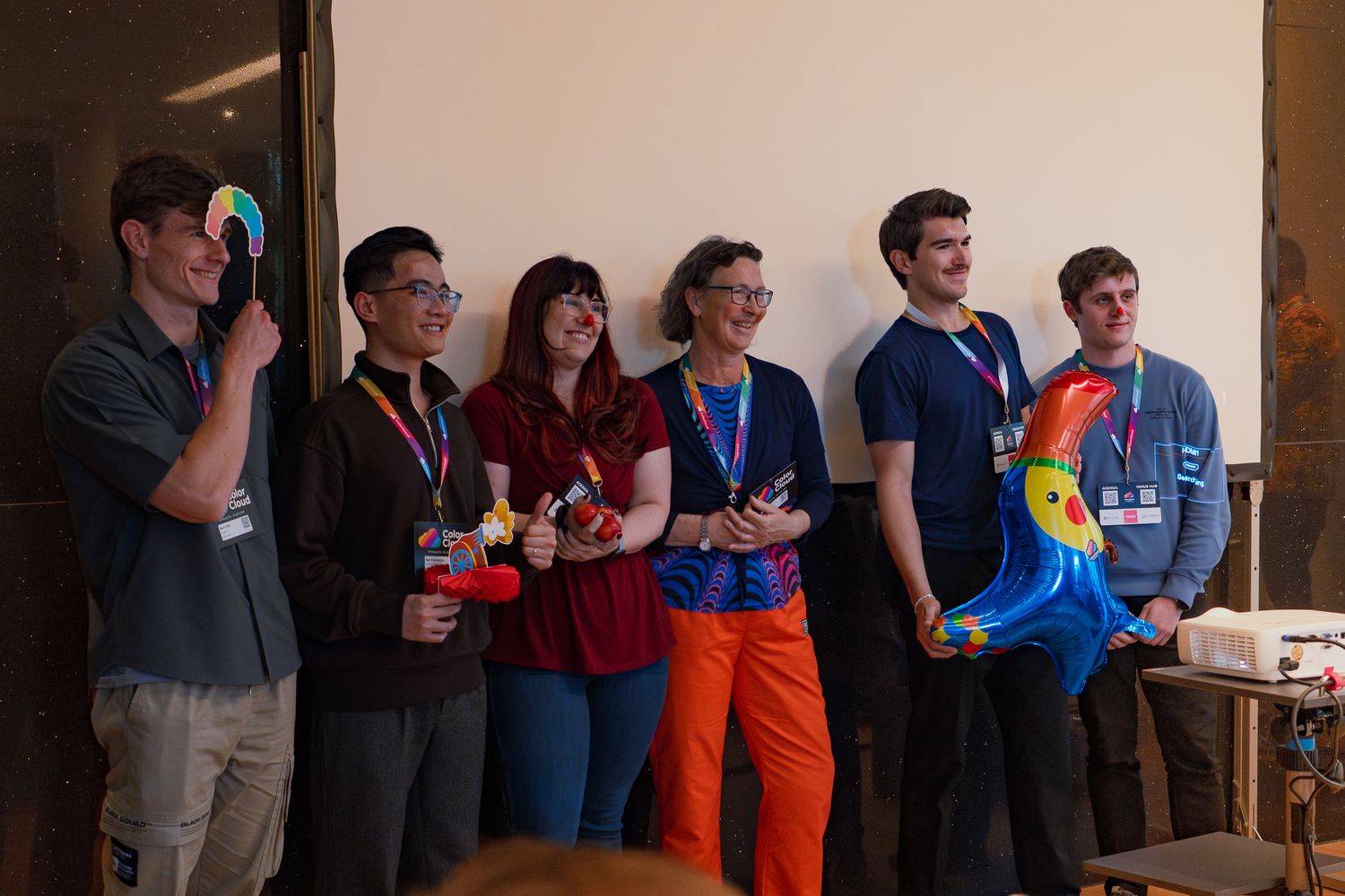Ein Team präsentiert beim ColorCloud PromptAthon Ergebnisse vor anderen Teilnehmenden und hält dabei bunte Luftballons in der Hand