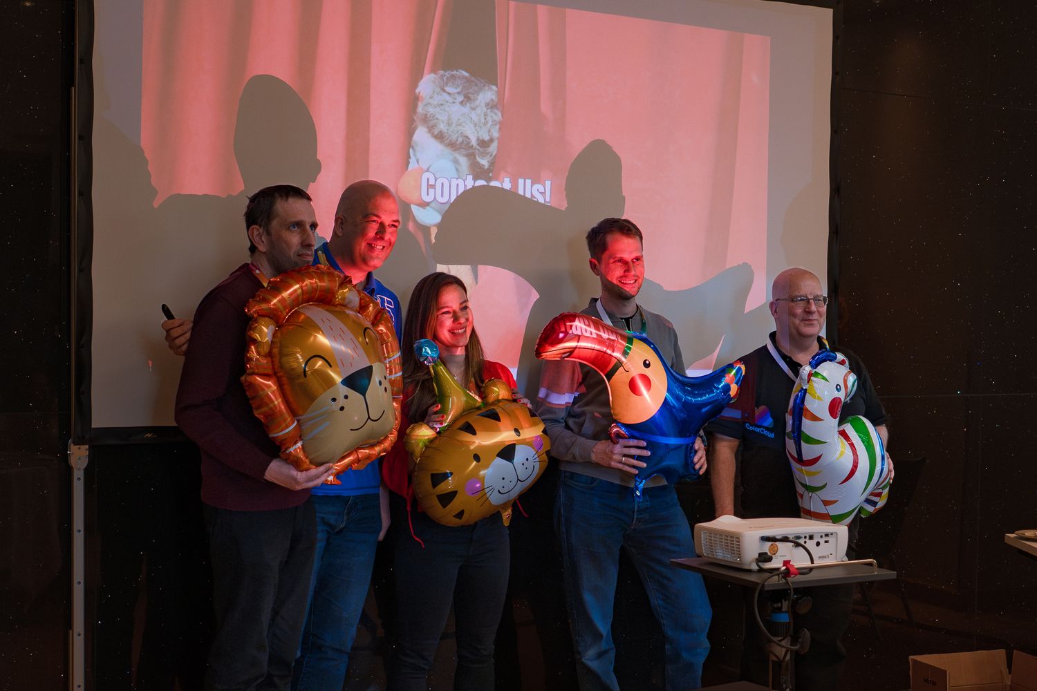 Ein Team präsentiert beim ColorCloud PromptAthon Ergebnisse vor anderen Teilnehmenden und hält dabei bunte Luftballons in der Hand