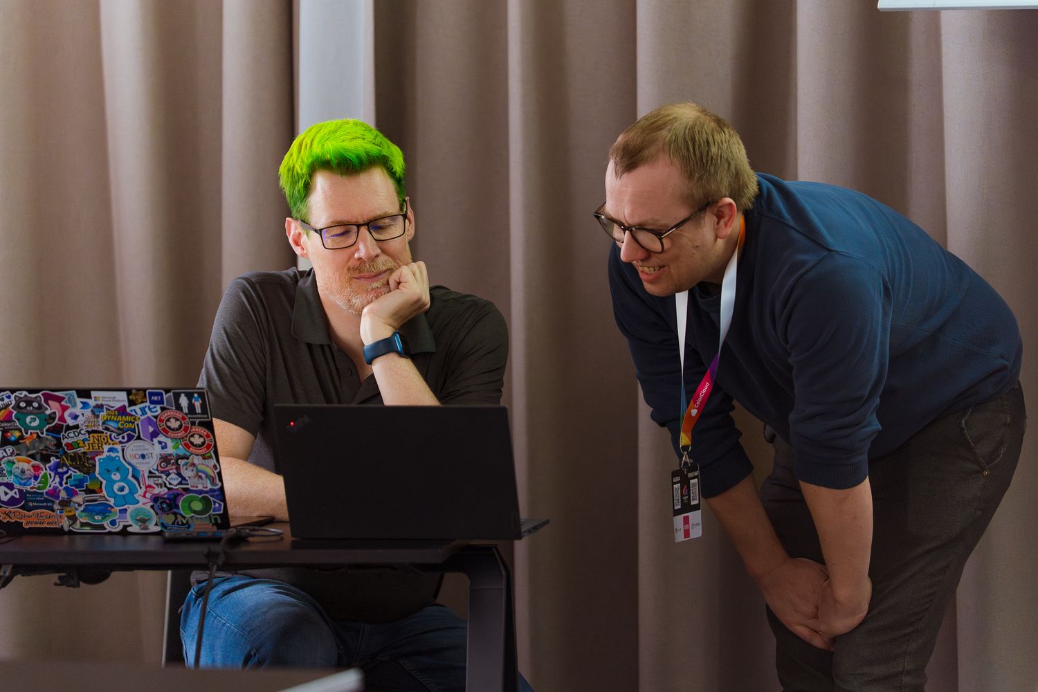Scott Durow mit grün gefärbten Haaren schaut zusammen mit einem Teilnehmer des ColorCloud-Workshops auf seinen Laptop