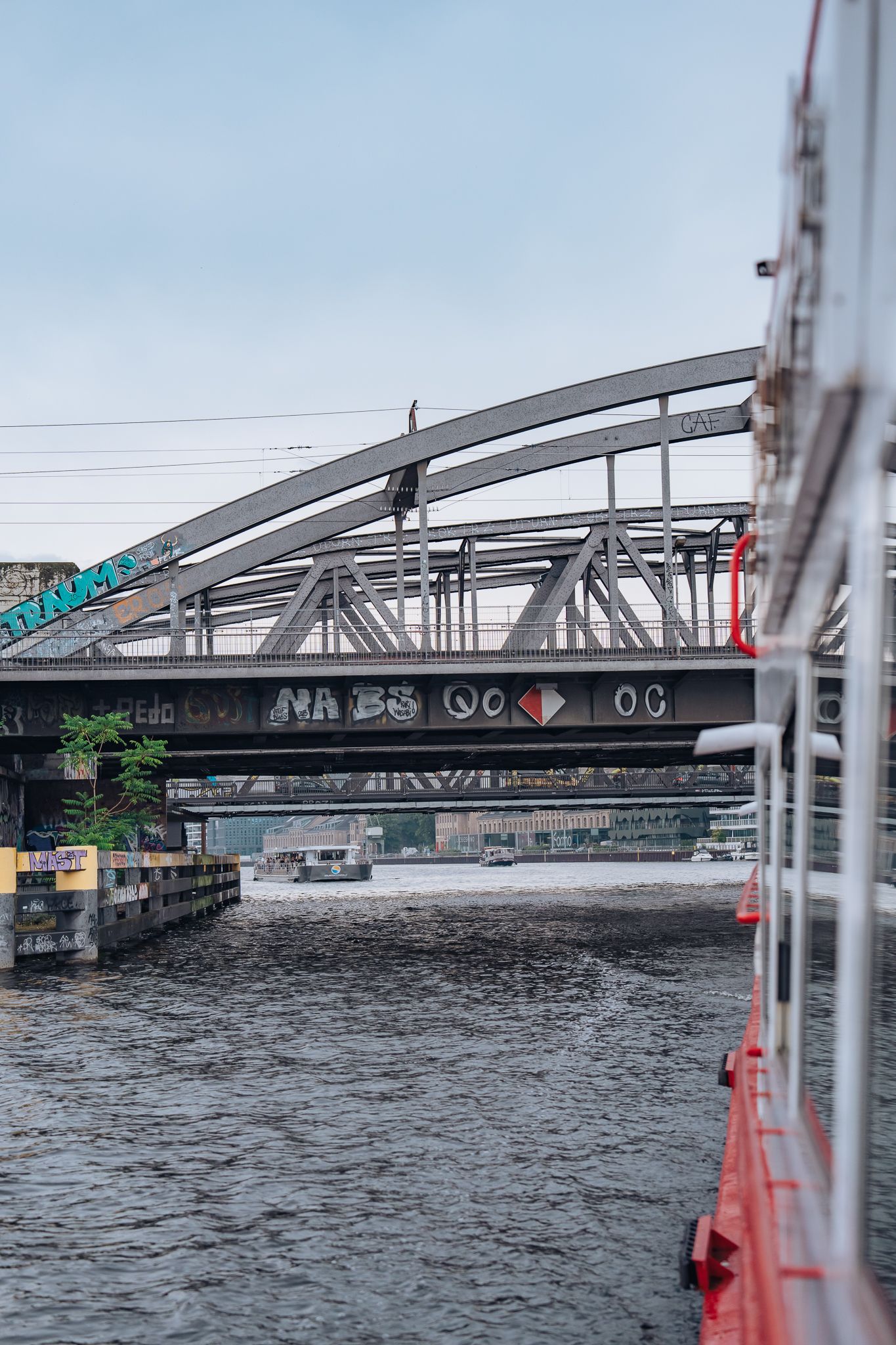 Stahlbahnbrücke über der Spree, im Hintergrund ein Ausflugsschiff und Graffiti an den Brückenträgern