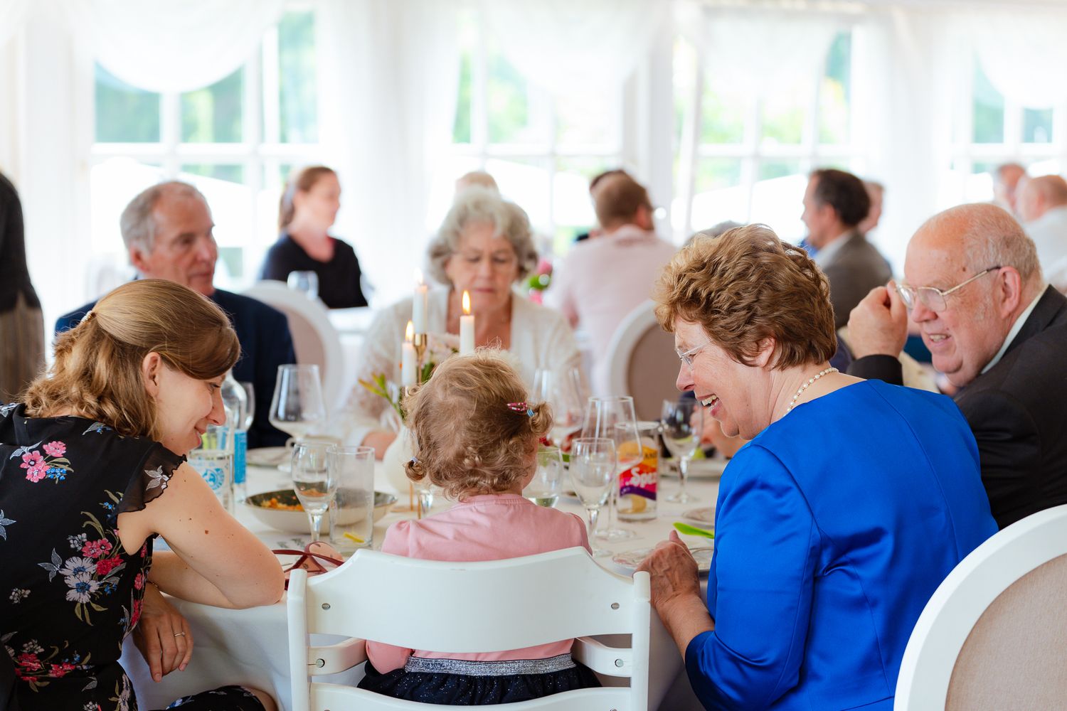 Oma und Mutter sprechen mit Kleinkind am weiß gedeckten Festtisch