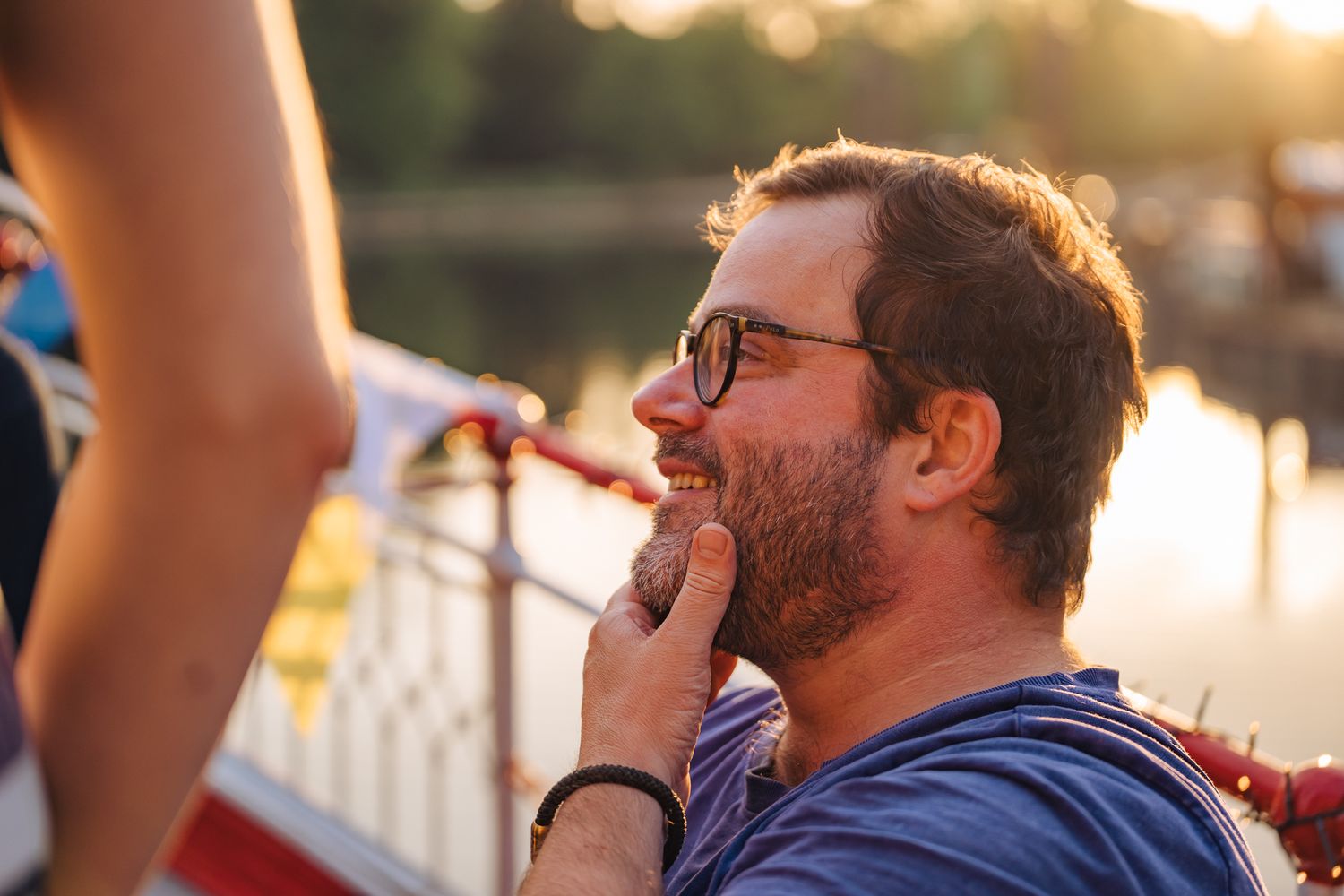 Mann mit Brille im Licht der Abendsonne hält sich den Bart