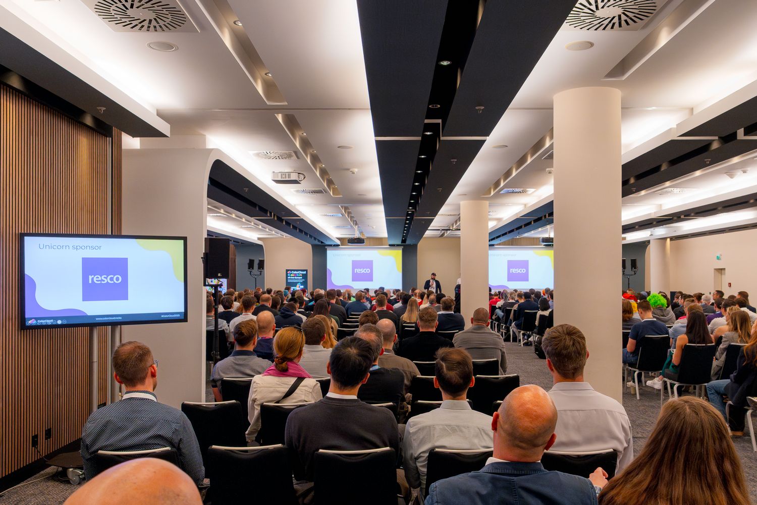 Jakub Bajla hält eine Rede vor den Teilnehmern der ColorCloud 2025, auf einem Monitor ist der Sponsor Resco zu sehen
