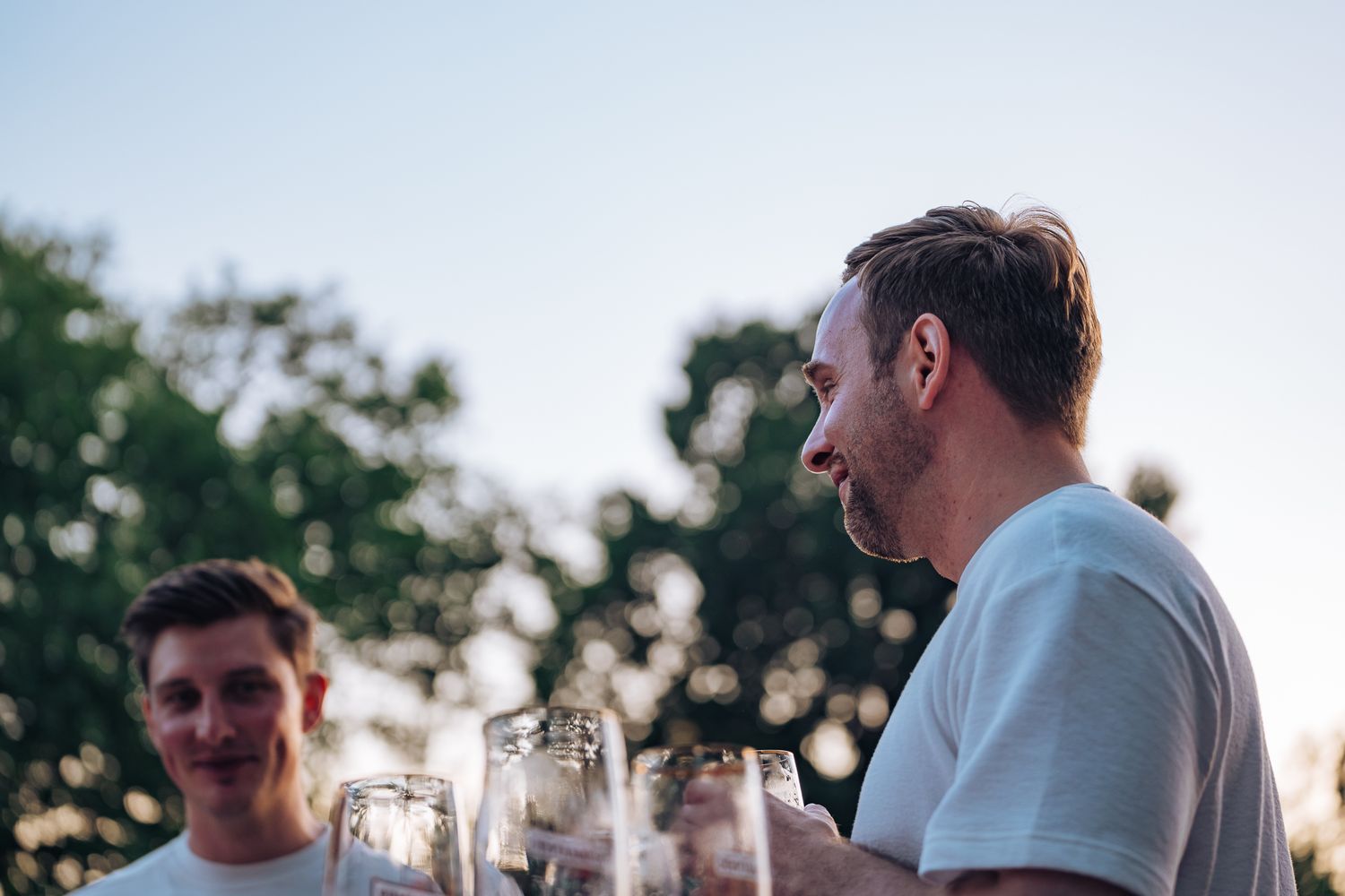 Drei Biergläser stehen im Vordergrund, im Hintergrund sind zwei Männer im weißen T-Shirt