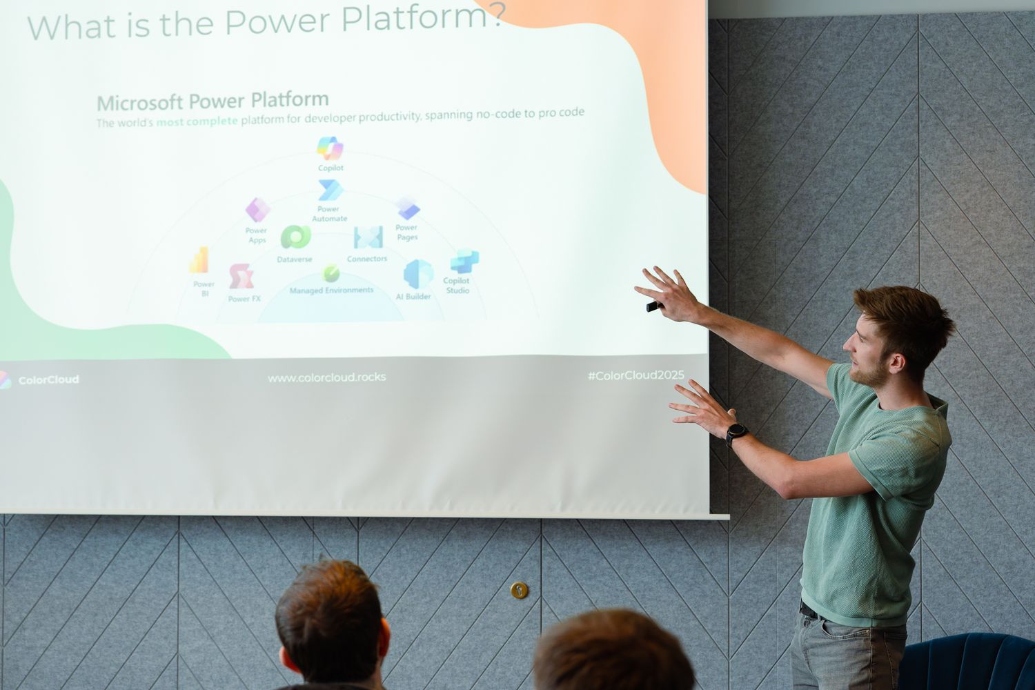 Tine Staric zeigt während seines Vortrags auf der ColorCloud mit zwei Händen auf eine Leinwand und stellt die Microsoft Power Platform vor