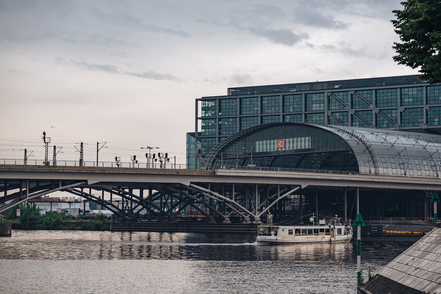 Berliner Hauptbahnhof mit verglastem Dach, Eisenbahnbrücke über der Spree und vorbeifahrendem Ausflugsschiff