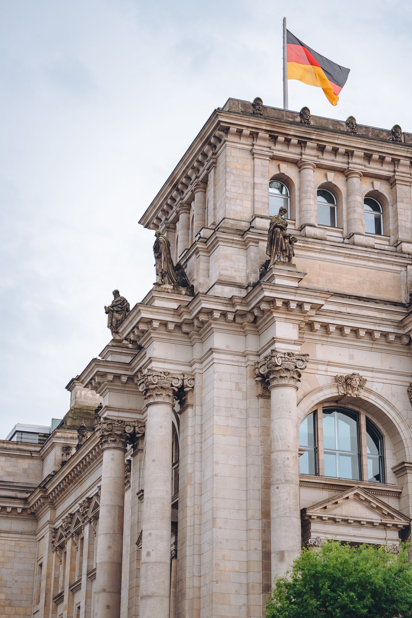 Fassade des Reichstags in Berlin mit Säulen, Statuen und deutscher Flagge auf dem Dach