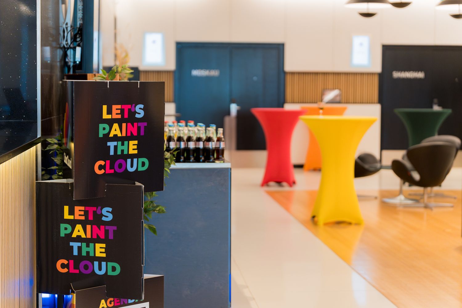Mehrere farbige Stehtische im Foyer des ColorClour-Workshoptags, daneben Schilder mit dem Schriftzug ‚Let’s Paint the Cloud‘