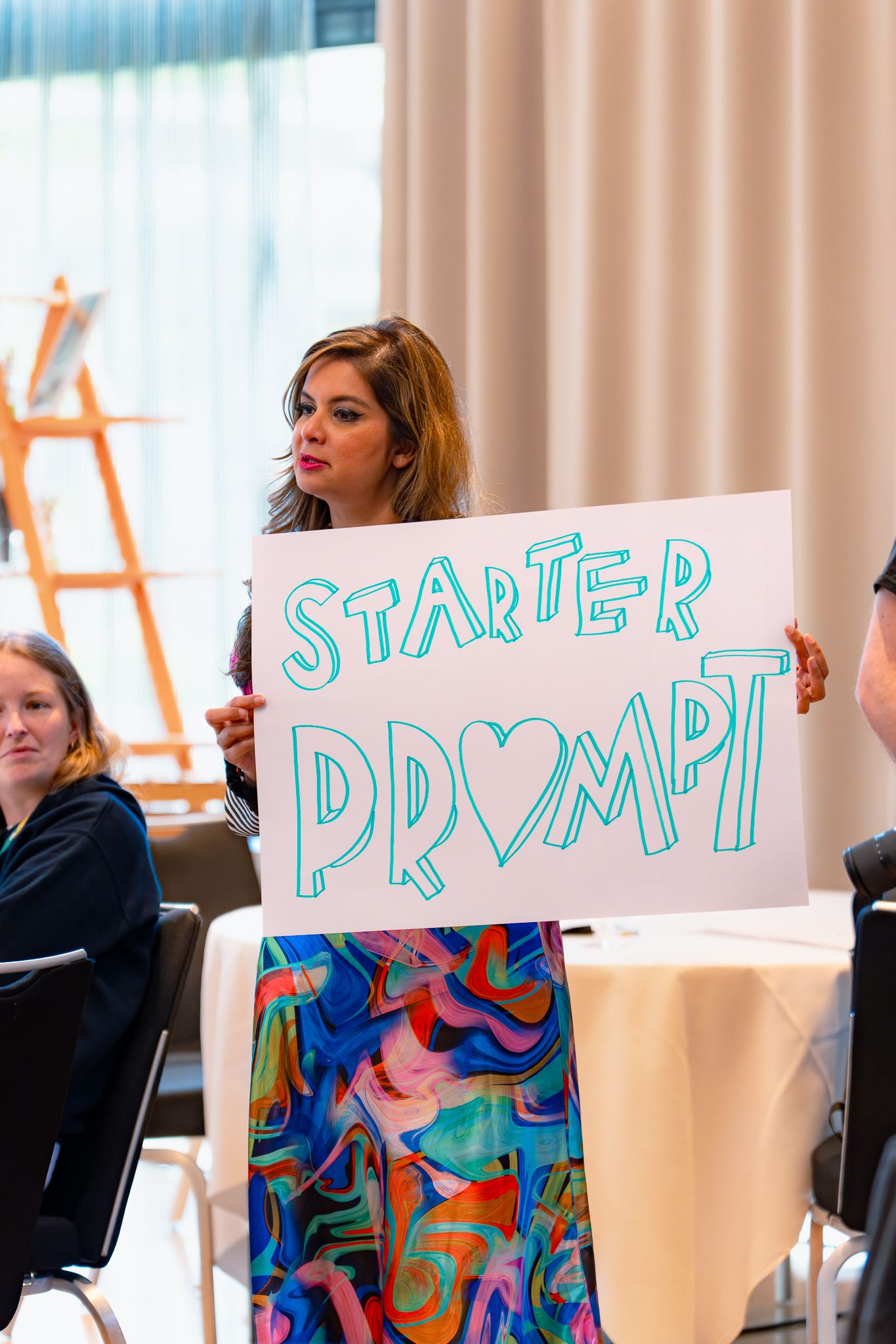 Dona Sarkar hält ein Schild mit der Aufschrift 'Starter Prompt' auf dem ColorCloud PromptAthon