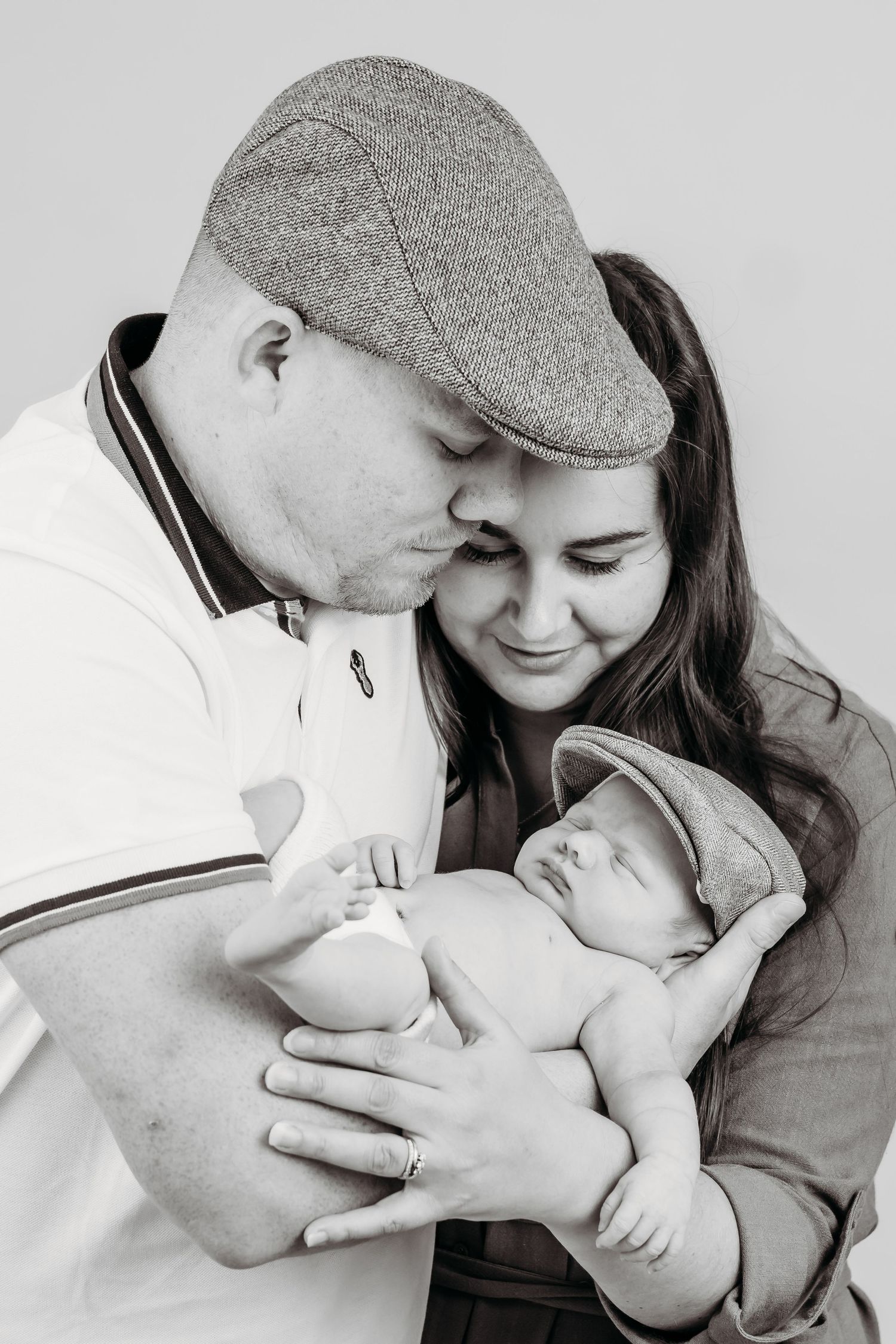 Intimate black and white portrait of new parents cradling their sleeping newborn baby.
