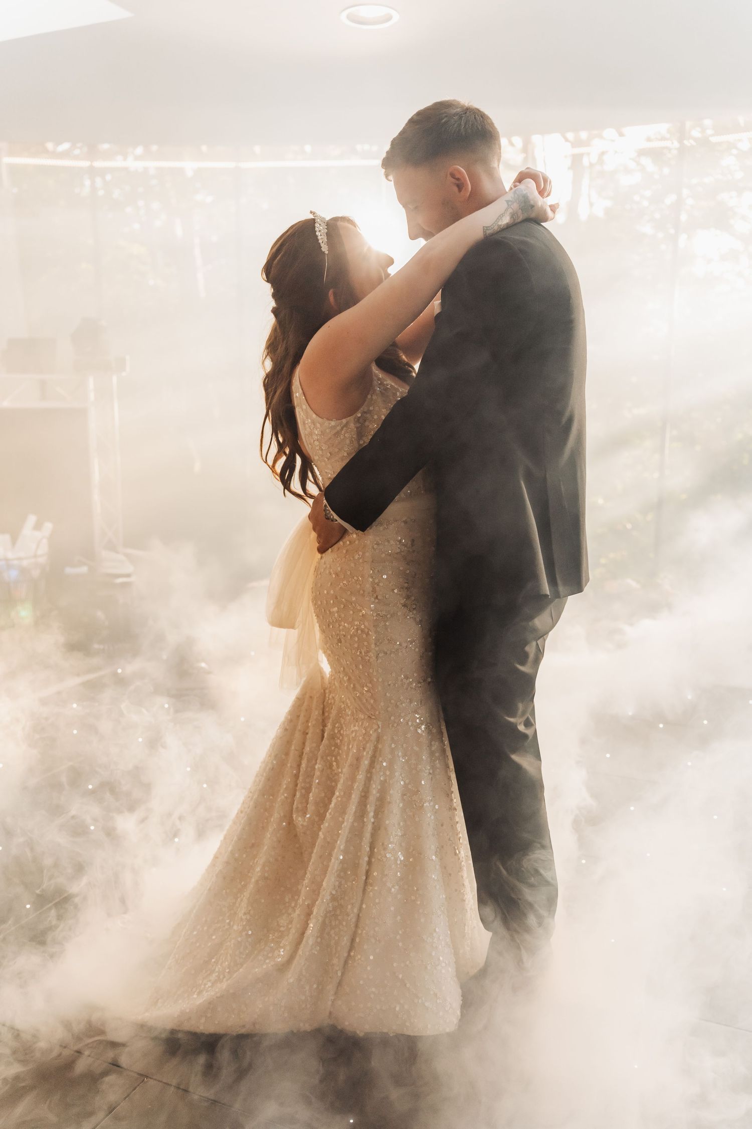 Bride and groom share first dance surrounded by dramatic fog clouds in elegant wedding venue.