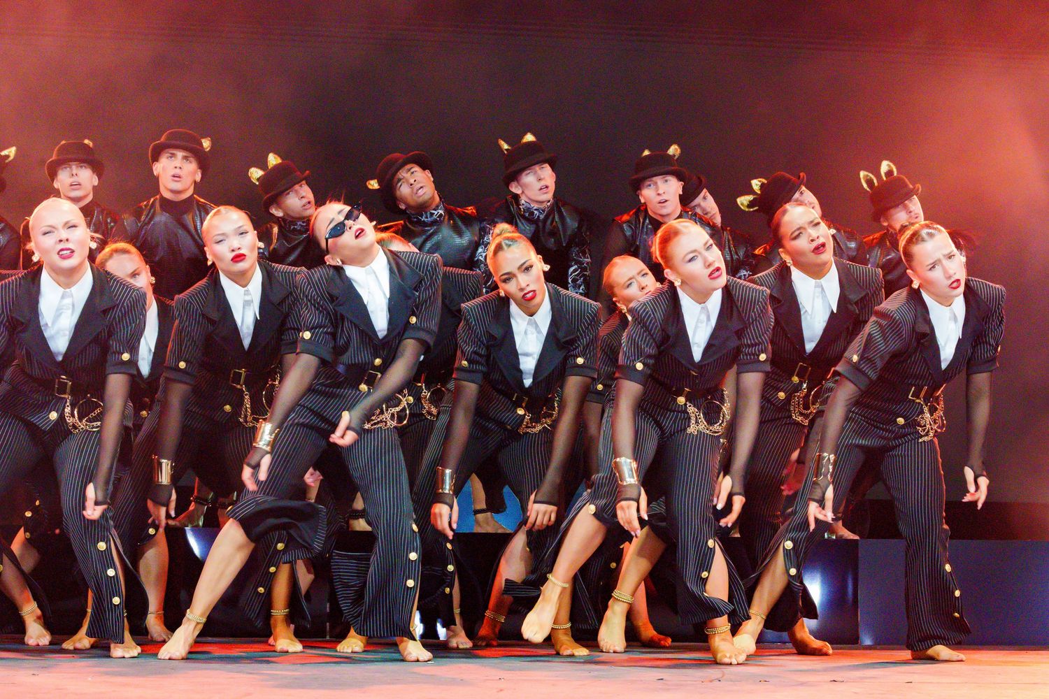 A group of dancers in black costumes perform a synchronized routine on a colorful stage.