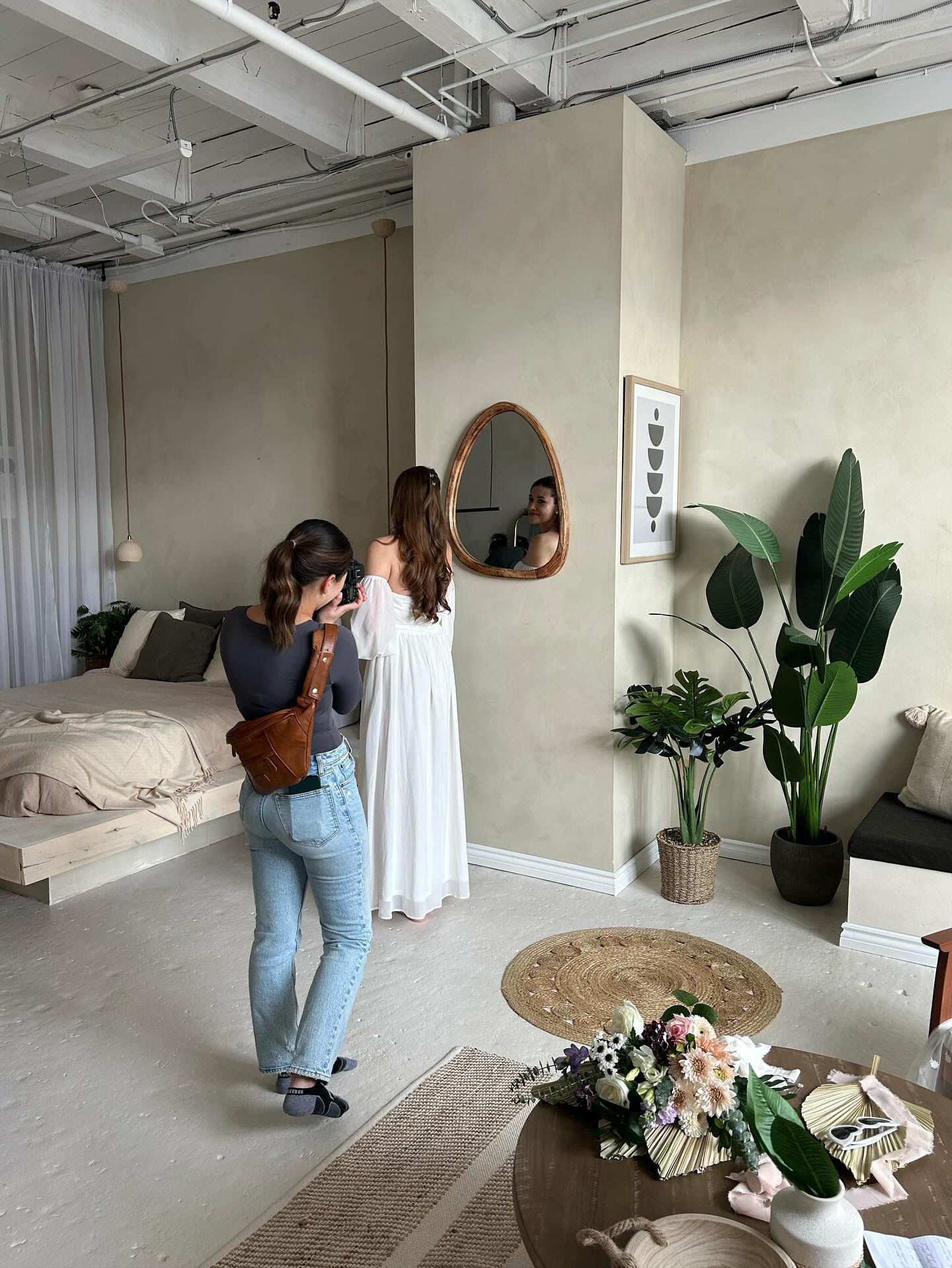 A photographer wearing blue jeans and a grey shirt taking a photo of a bride in a wedding dress with puffy sleeves. The 