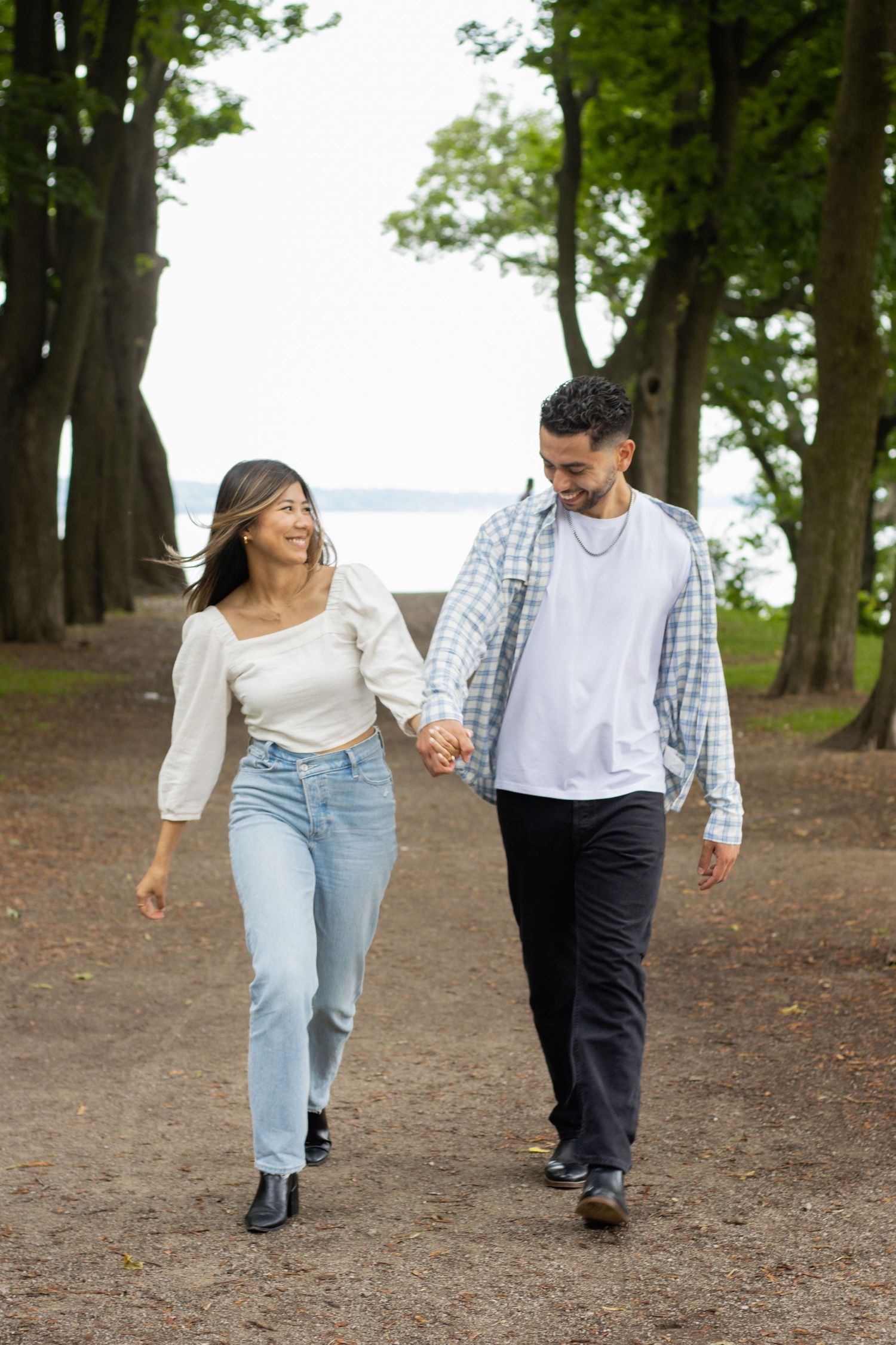 Man and woman walking hand and hand down a tree covered path.